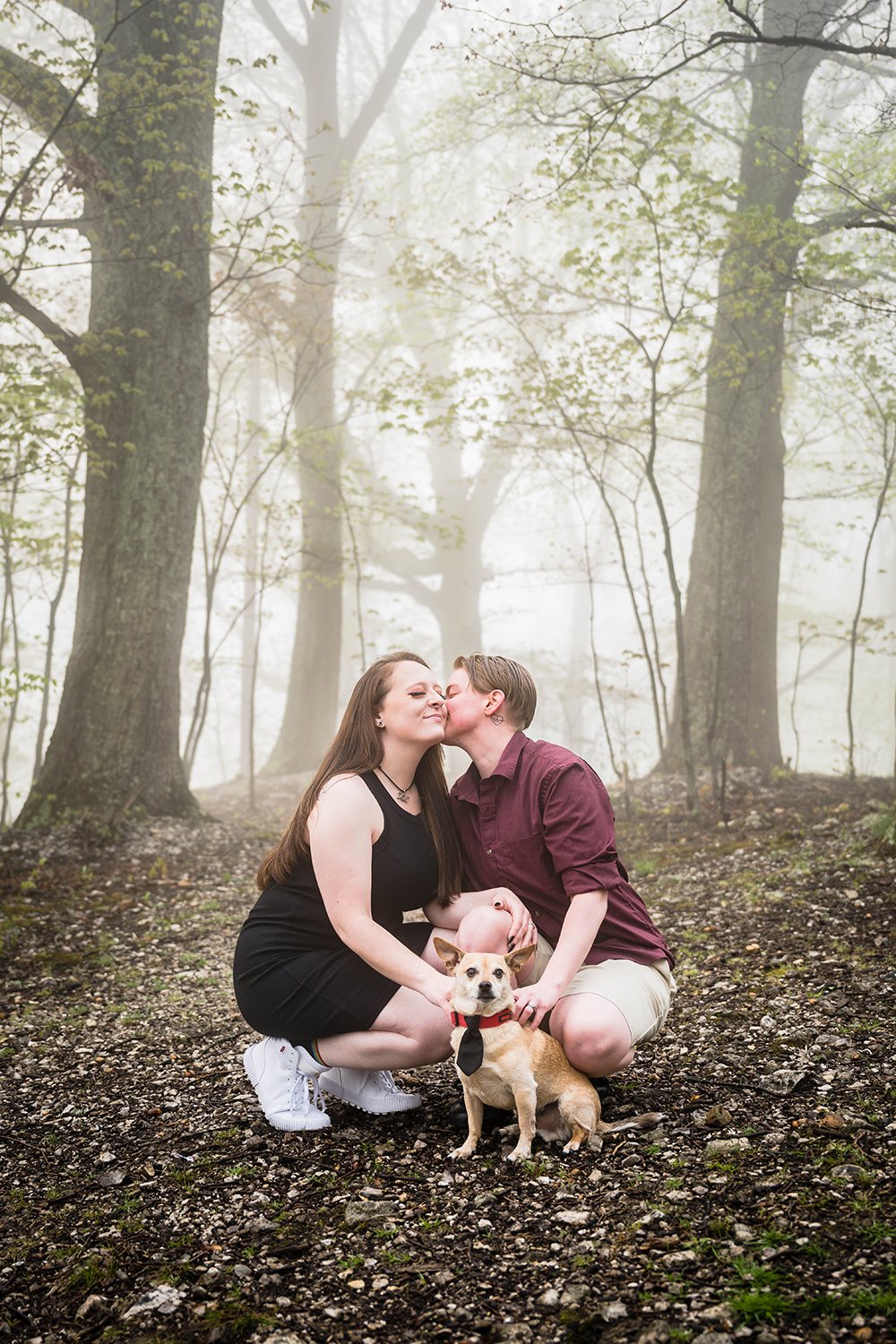 A person kisses their partner while holding onto their dog during their engagement session in Virginia.