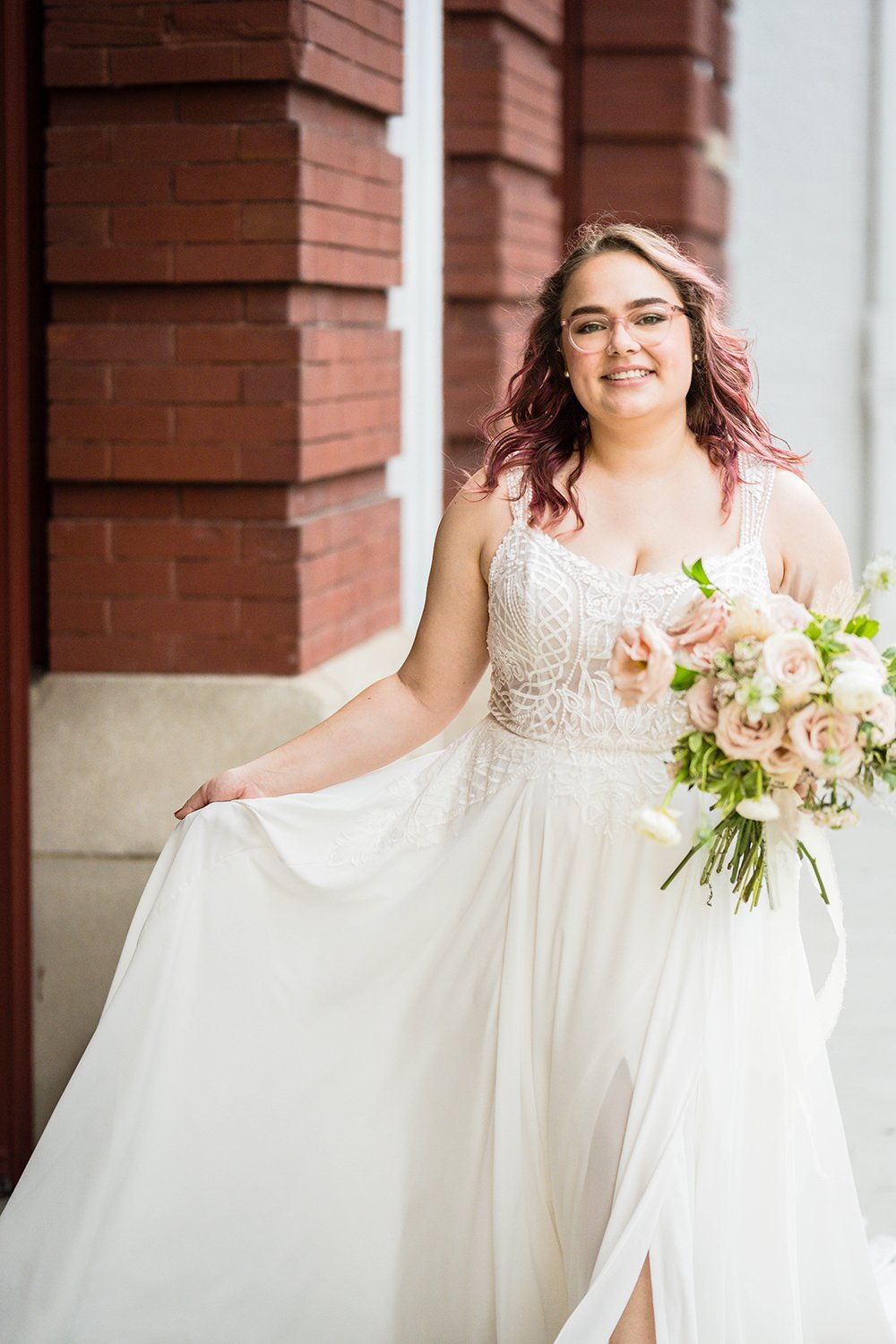 A marrier walks in front of the Fire Station One Boutique Hotel in Downtown Roanoke while holding their dress in one hand and their wedding bouquet in the other hand.