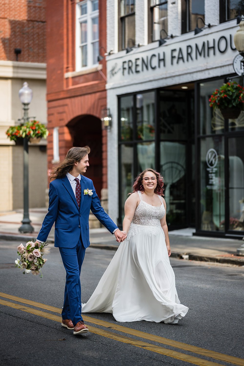 A newlywed couple holds hands and walks on an empty street in Roanoke, Virginia featuring the Fire Station One Hotel and the French Farmhouse.