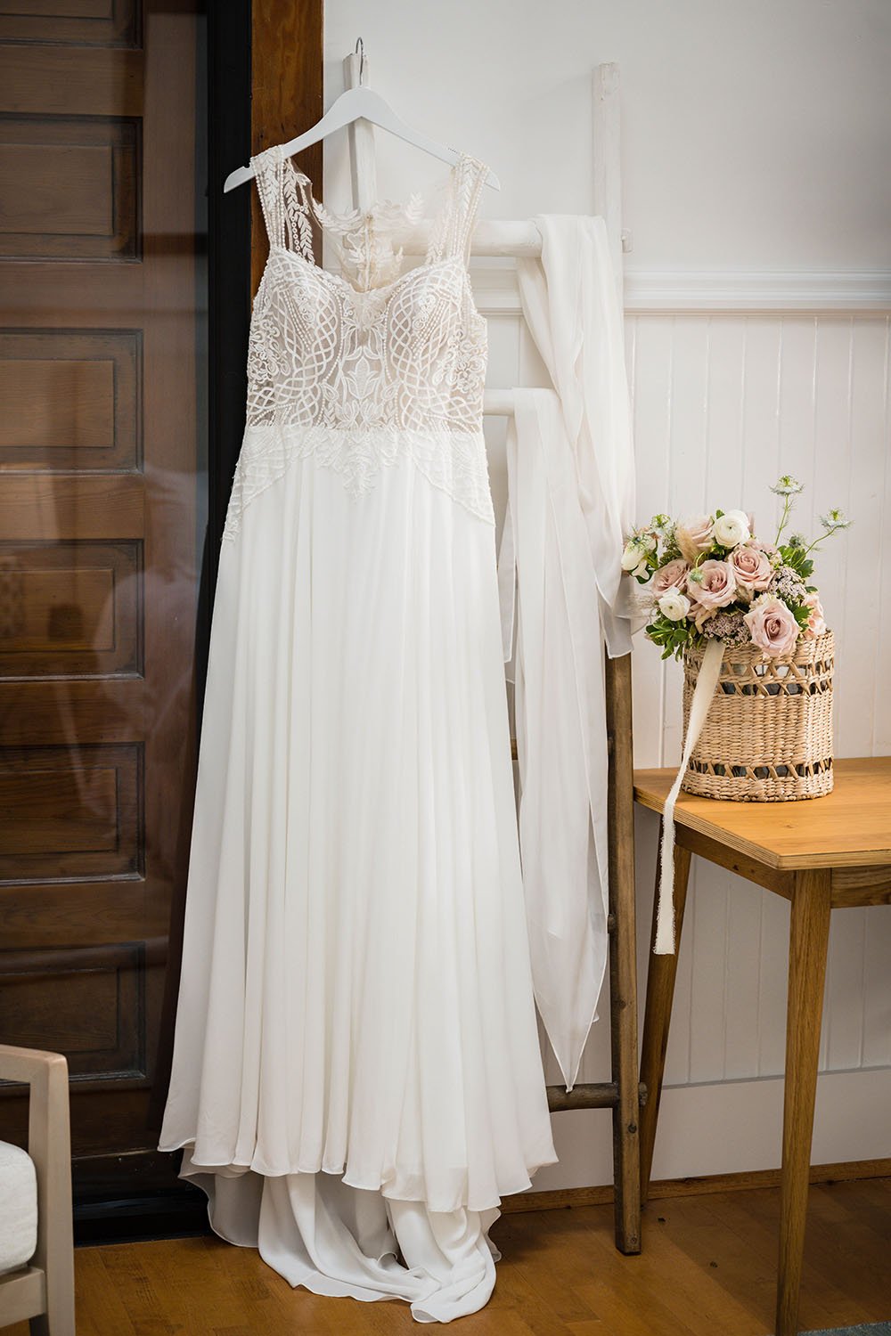 A wedding dress with its streamers are hung upon a white ladder in the Cottage Room at the Fire Station One Boutique Hotel in Downtown Roanoke. Next to the dress is the bride's wedding bouquet.