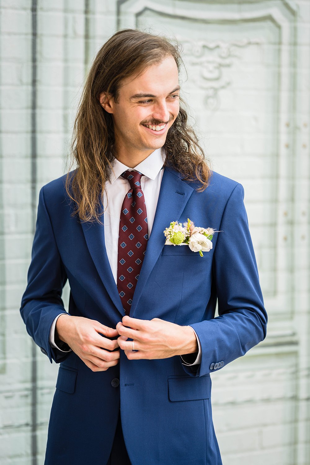 A marrier buttons his suit jacket as he looks off camera and smiles near the Fire Station One Hotel in Roanoke, Virginia.