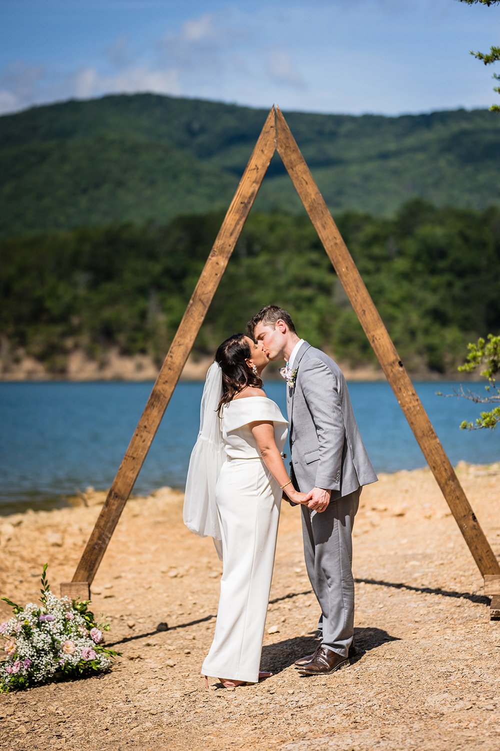 Two marriers stand underneath a triangle wooden arch and go in for their first kiss during their elopement at Carvin’s Cove in Roanoke, Virginia.