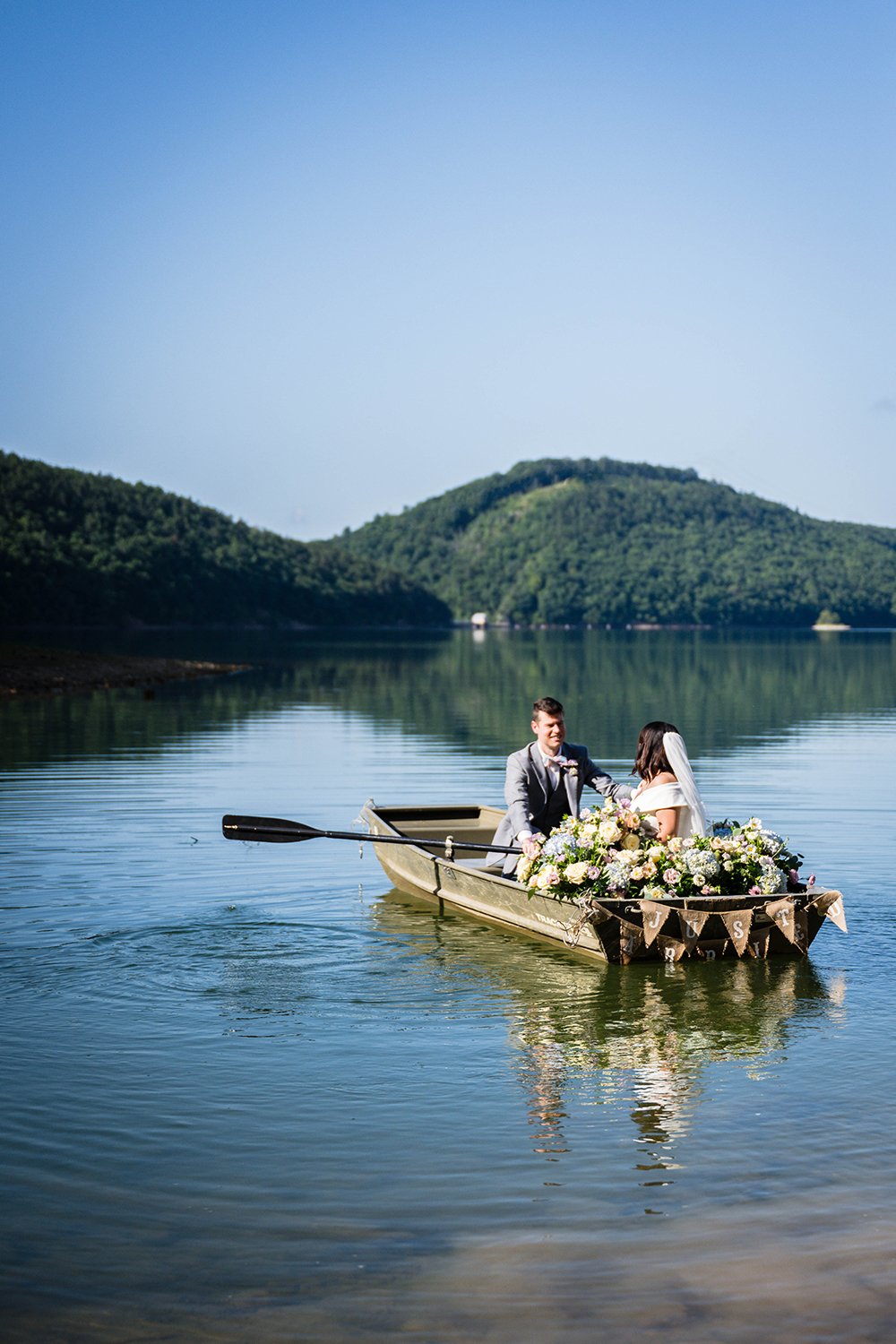 A wedding couple embark on a row boat adorned with boat florals into Carvin’s Cove in Roanoke, Virginia during their elopement.