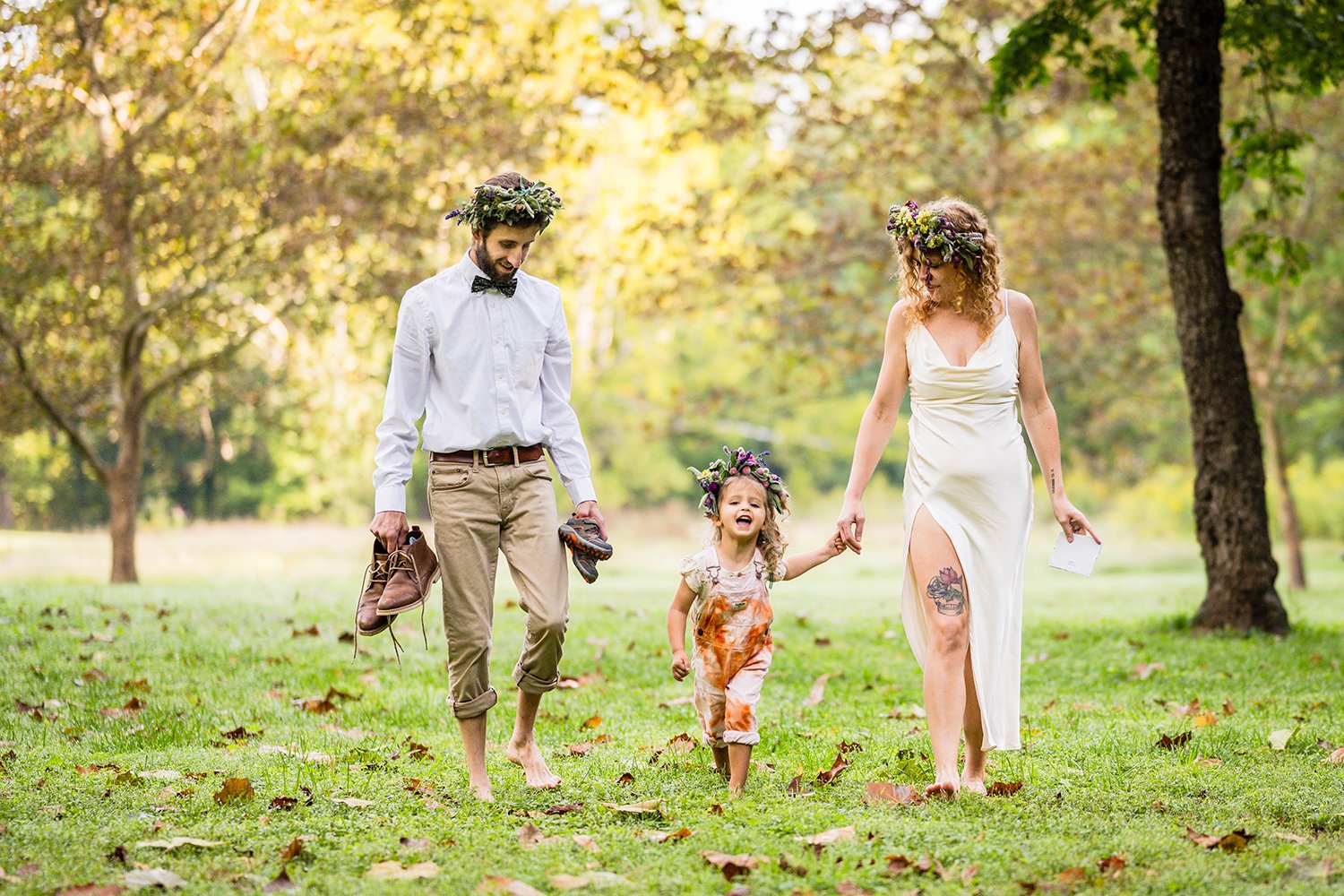 A bride and groom walk hand in hand with their child in a park towards their ceremony location on their elopement day in Virginia.