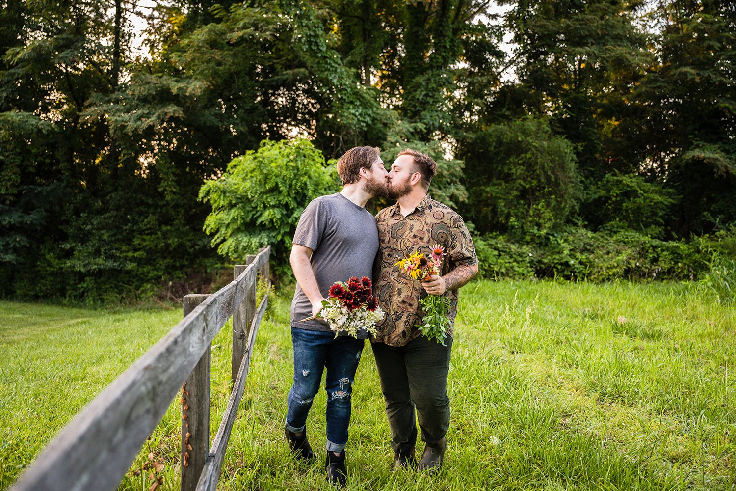 The owners of Fae Cottage Flower hold flowers plucked from their garden and kiss one another during their adventure session in Roanoke, Virginia.
