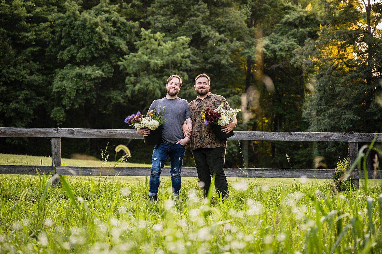 A gay couple holds a bucket of flowers from Fae Cottage Flower Farms and pose for a photo during a couple's session.