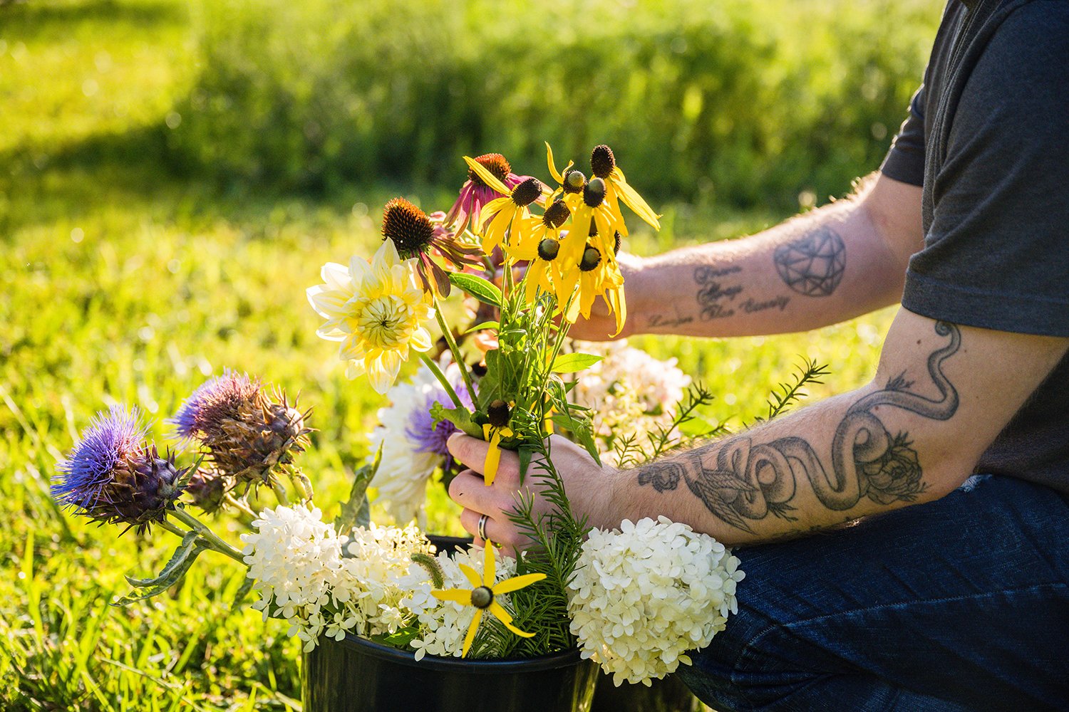 A close up shot of a person’s arms taking out a few flowers out of a bucket during a photo session at Fae Cottage Flower Farm.