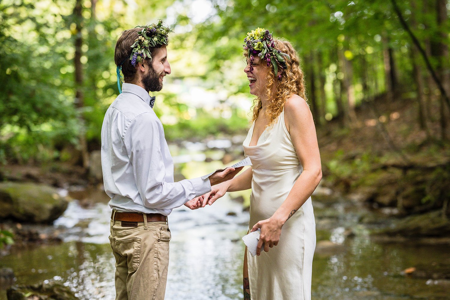 An LGBTQ+ couple stands in the creek at Fishburn Park to read their vows during their elopement.