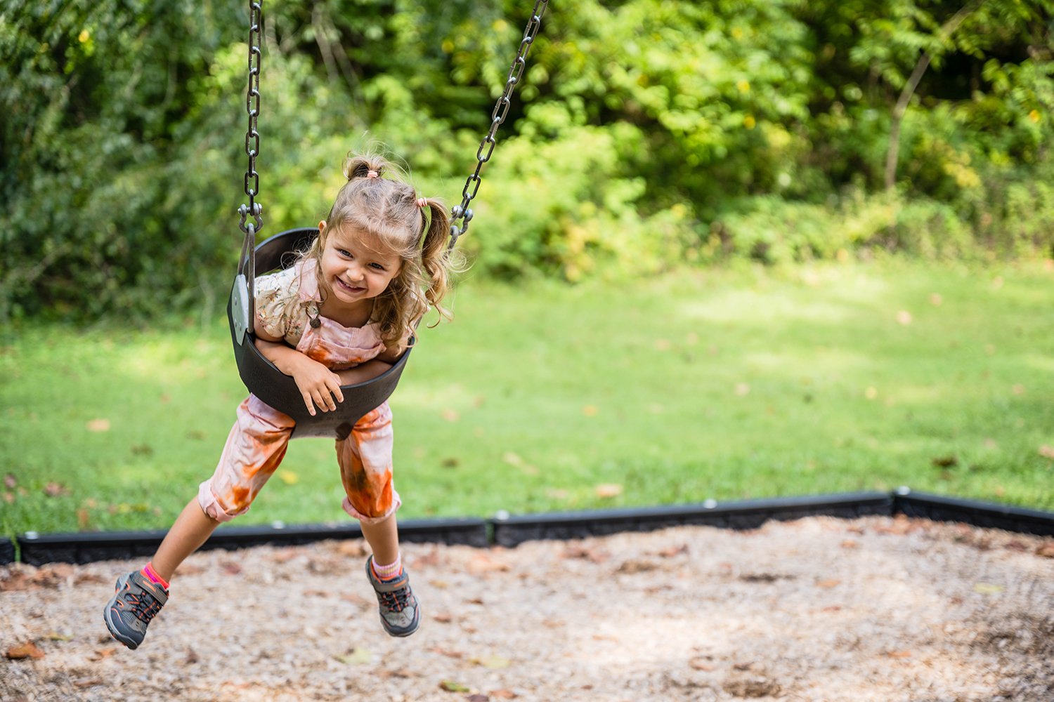 A toddler in a swing smiles as she is pushed into the air.
