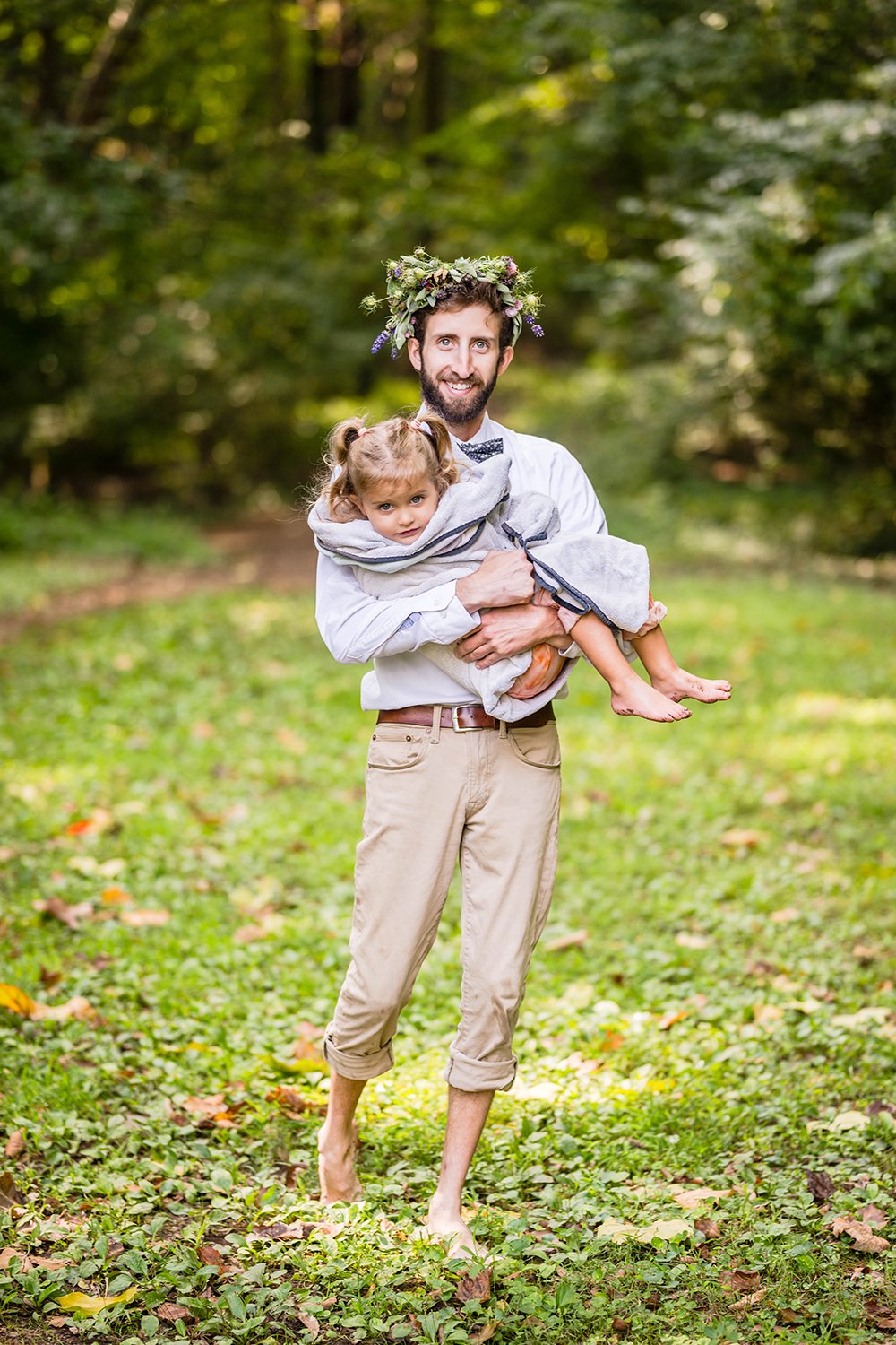 A father smiles and walks holding his daughter wrapped in a towel.