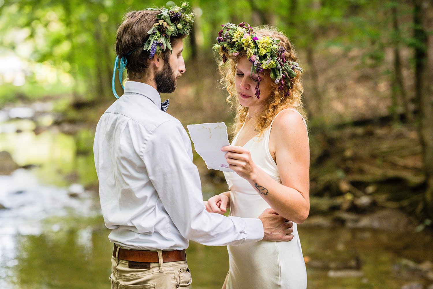 An LGBTQ+ couple stands in the creek at Fishburn Park to read their vows during their elopement.