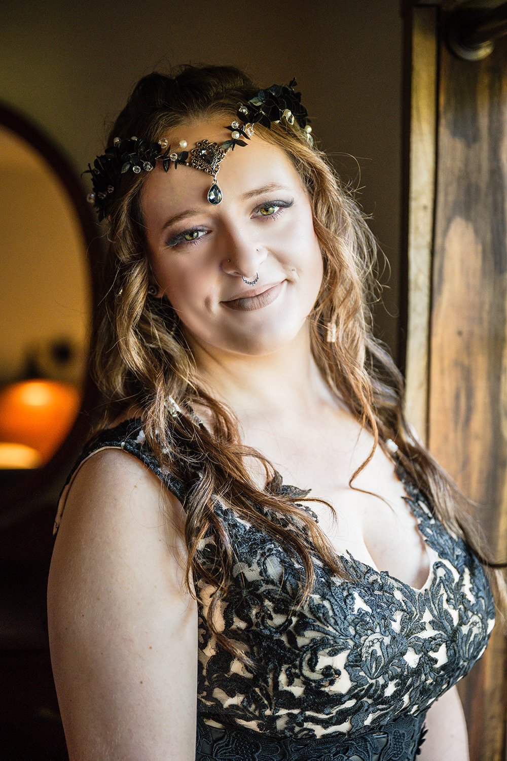 A lesbian marrier wearing a black wedding dress and a black headpiece stands against a window inside of a Roanoke Airbnb on her elopement day.