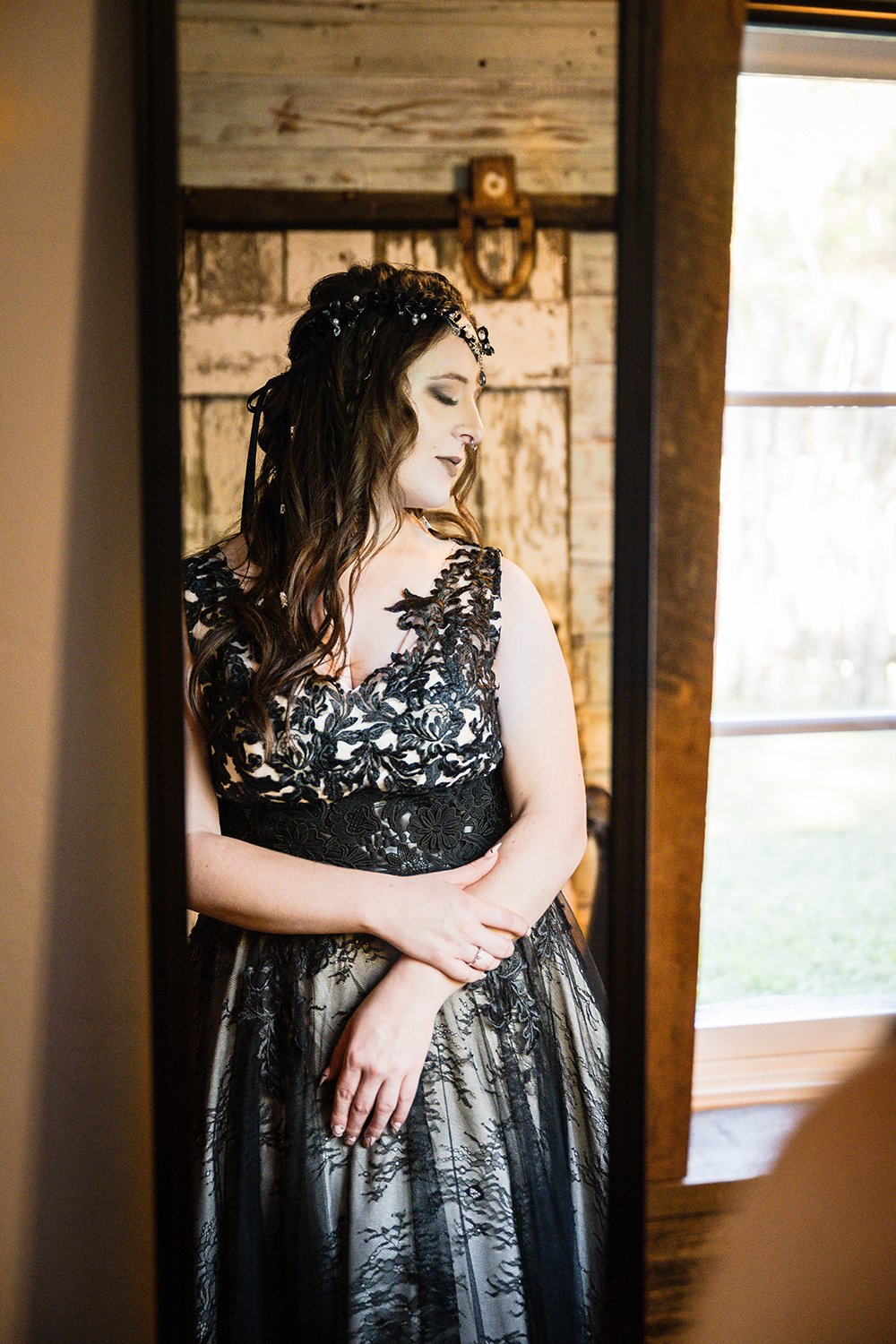 A lesbian marrier wearing a black wedding dress and a black headpiece stands in front of a mirror inside of a Roanoke Airbnb on her elopement day.