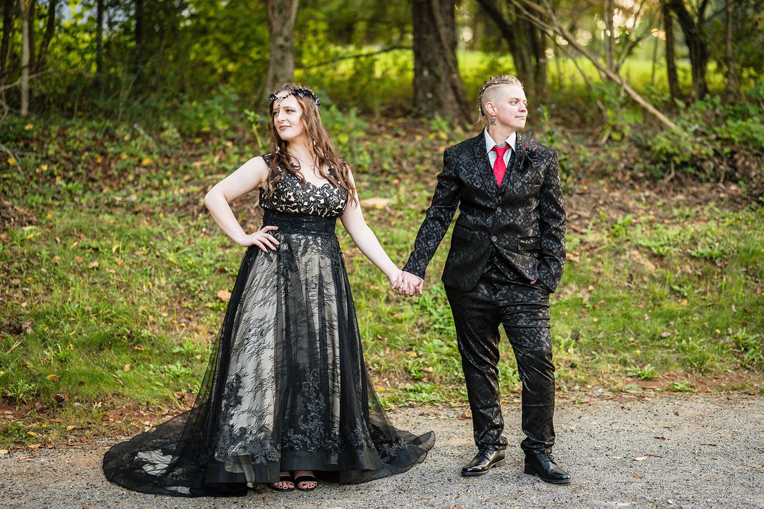 A lesbian bride wearing a black wedding dress and another queer marrier wearing a black floral suit stand hand in hand and look opposite directions during their Roanoke airbnb elopement.