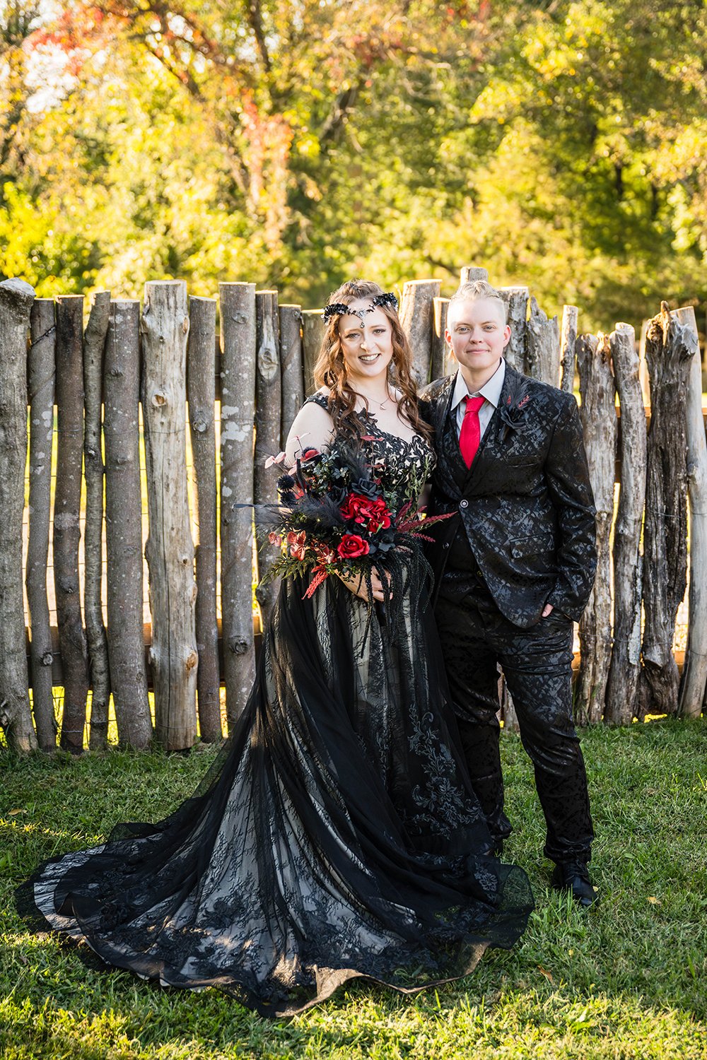 A queer couple stands together both wearing black inside the yard during their elopement for a formal portrait.