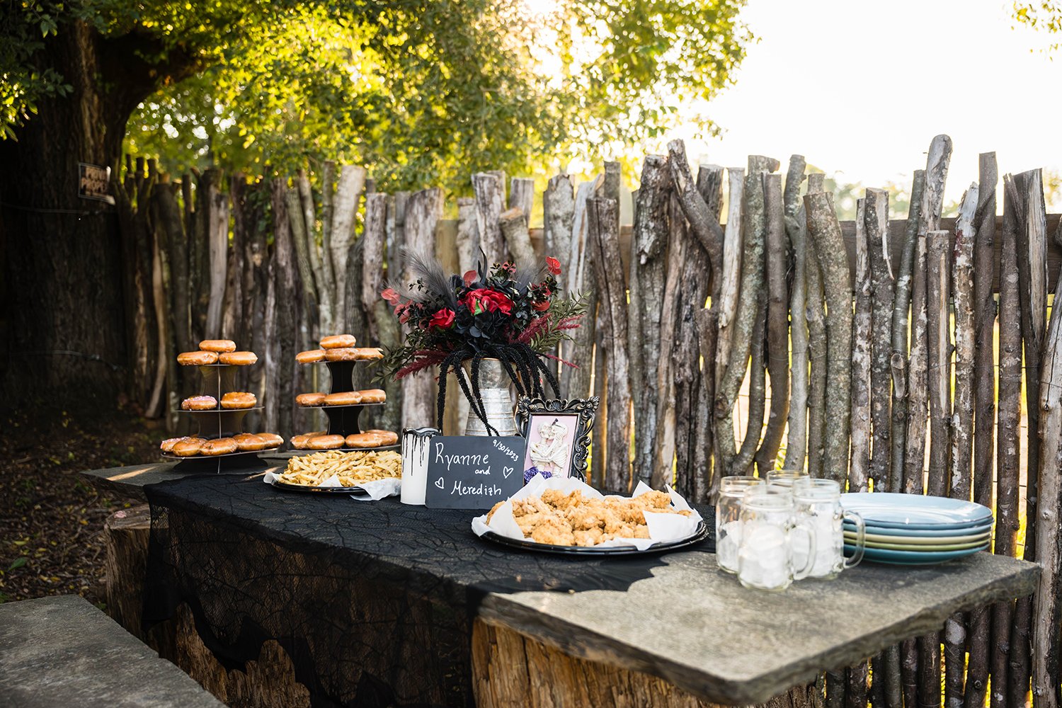 A stone table sits is decorated with a black tablecloth and features plates, glasses, platters of chicken tenders and fries, and Krispy Kreme donut towers at a Roanoke Airbnb.