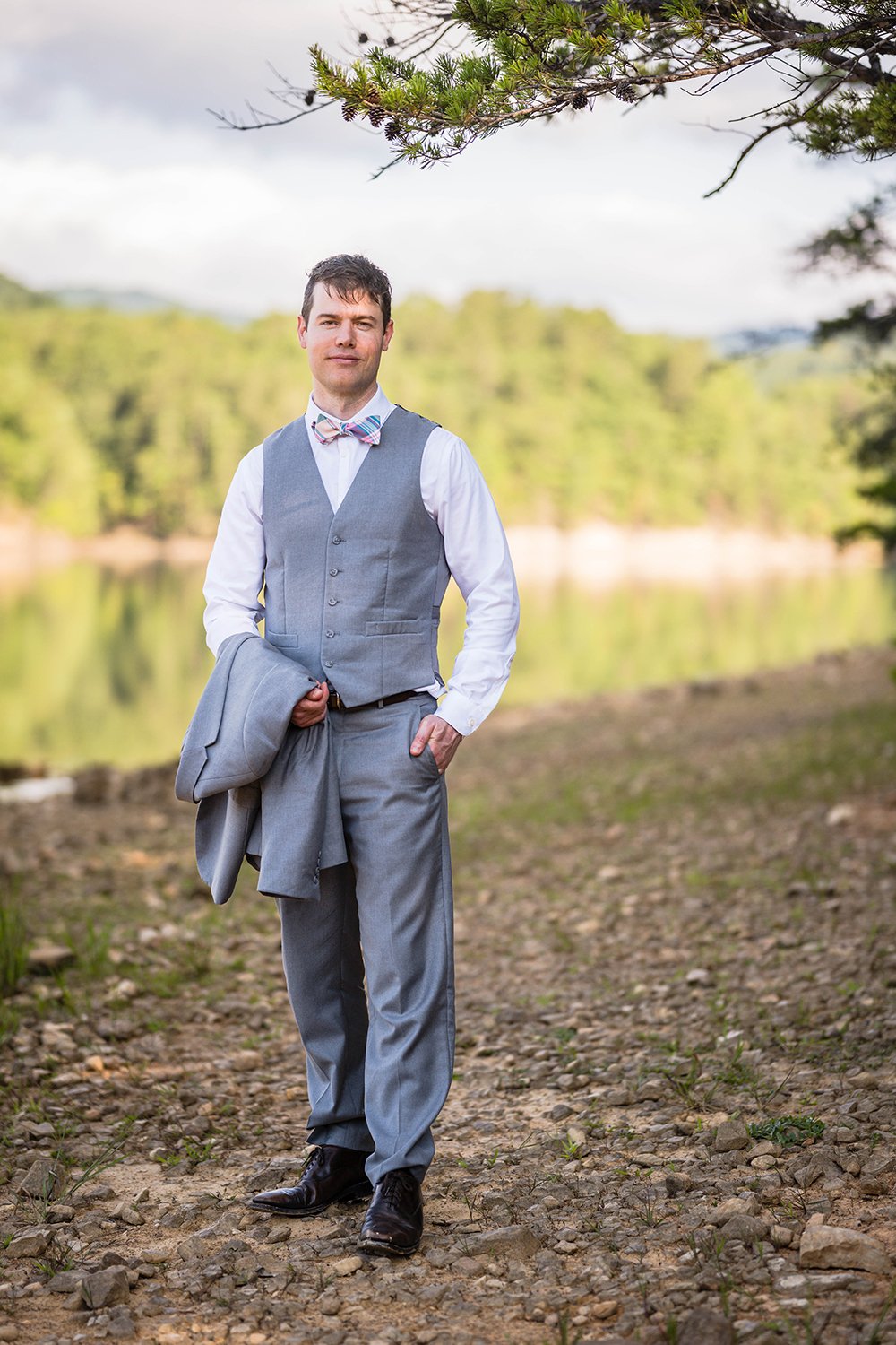 A man on his elopement day stands holding his suit jacket and looks at the camera for a photo.