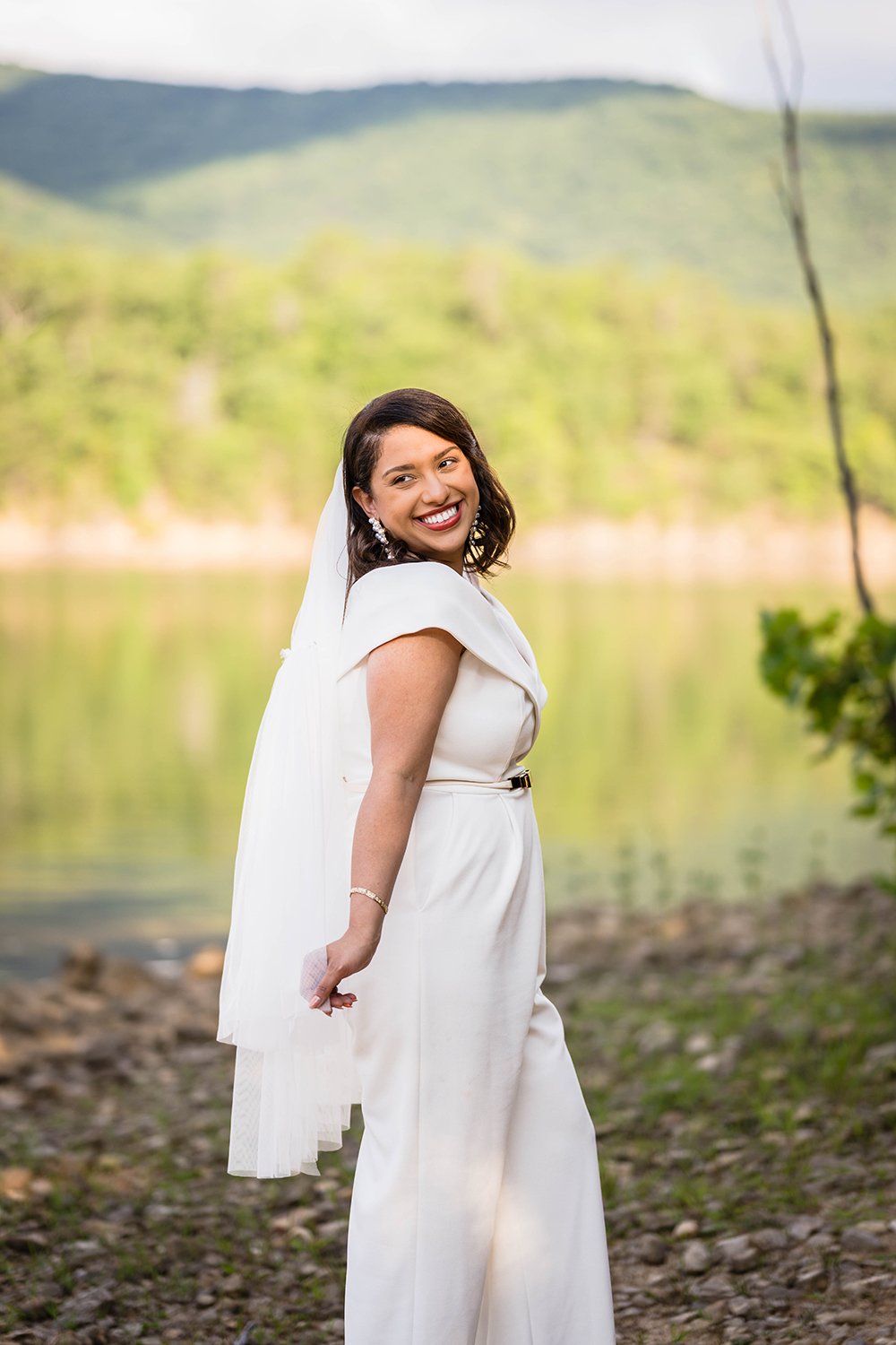 A smiling bride sports a wedding jumpsuit and veil and smiles big for the camera in Roanoke, Virginia, a town along the Blue Ridge Parkway.