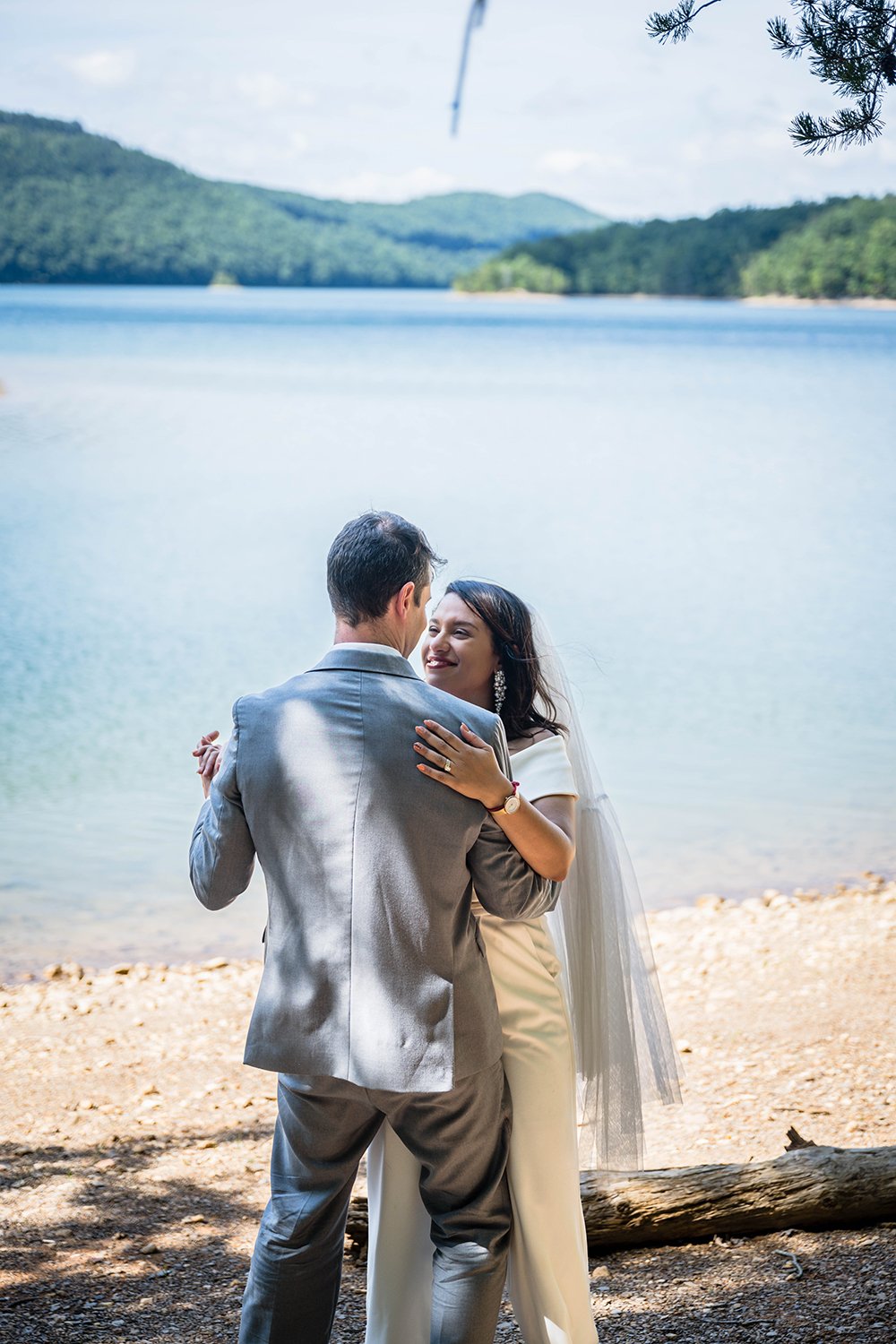 A newlywed couple take their first dance on the coast of Carvin's Cove with a blue lake and the Blue Ridge Mountains as their backdrop on their elopement day.