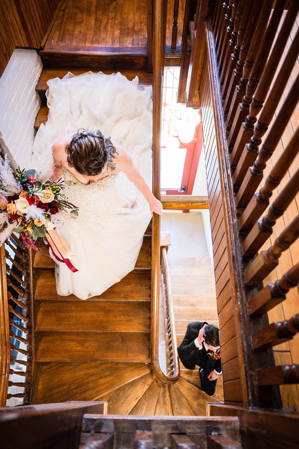A marrier in her wedding dress with her bouquet walks down the stairs of the Fire Station One hotel as her partner walks up the stairs for their first look on their elopement day.