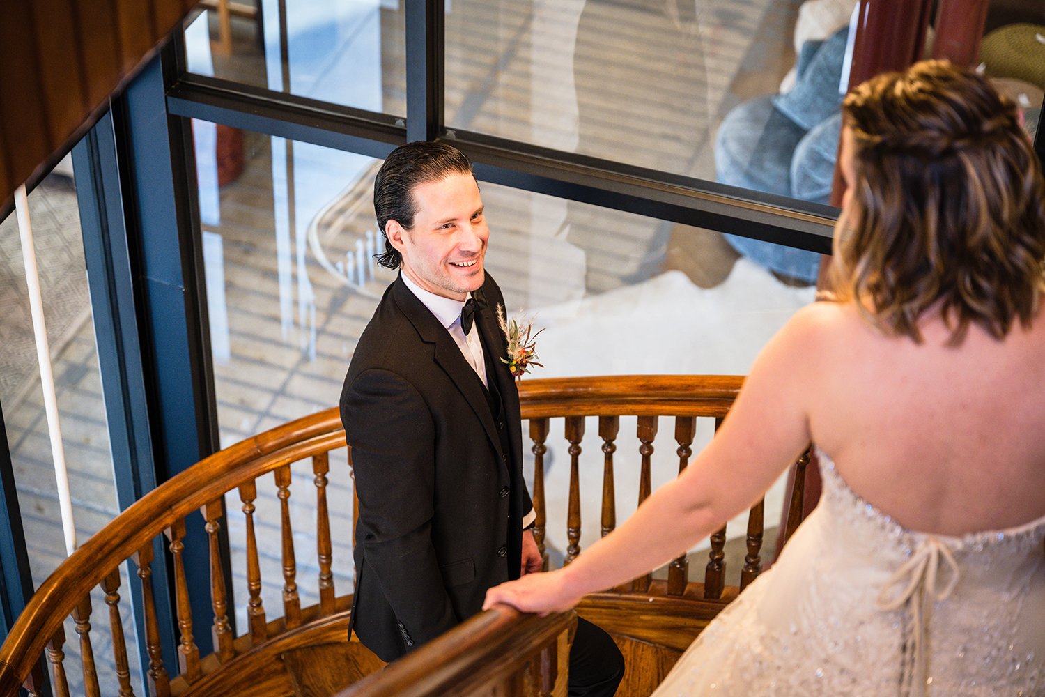 A groom smiles widely on his elopement as his soon-to-be wife comes down the stairwell at Fire Station One in her wedding dress.