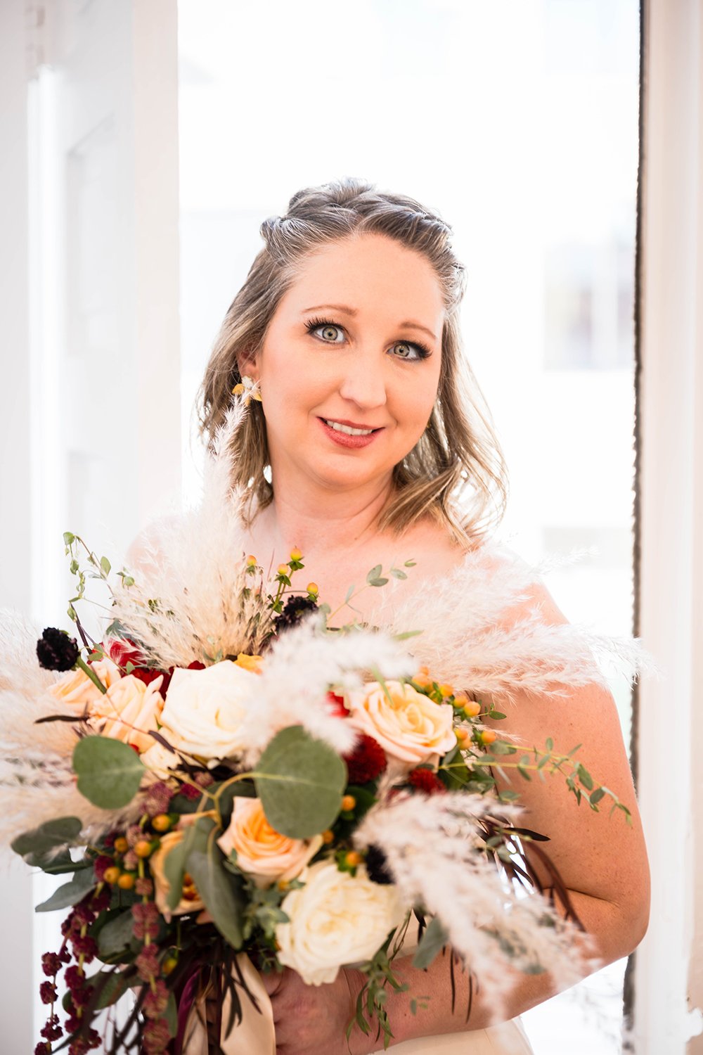 A bride on her elopement day holds a bouquet of flowers up for a photo in her hotel room at Fire Station One in Downtown Roanoke.