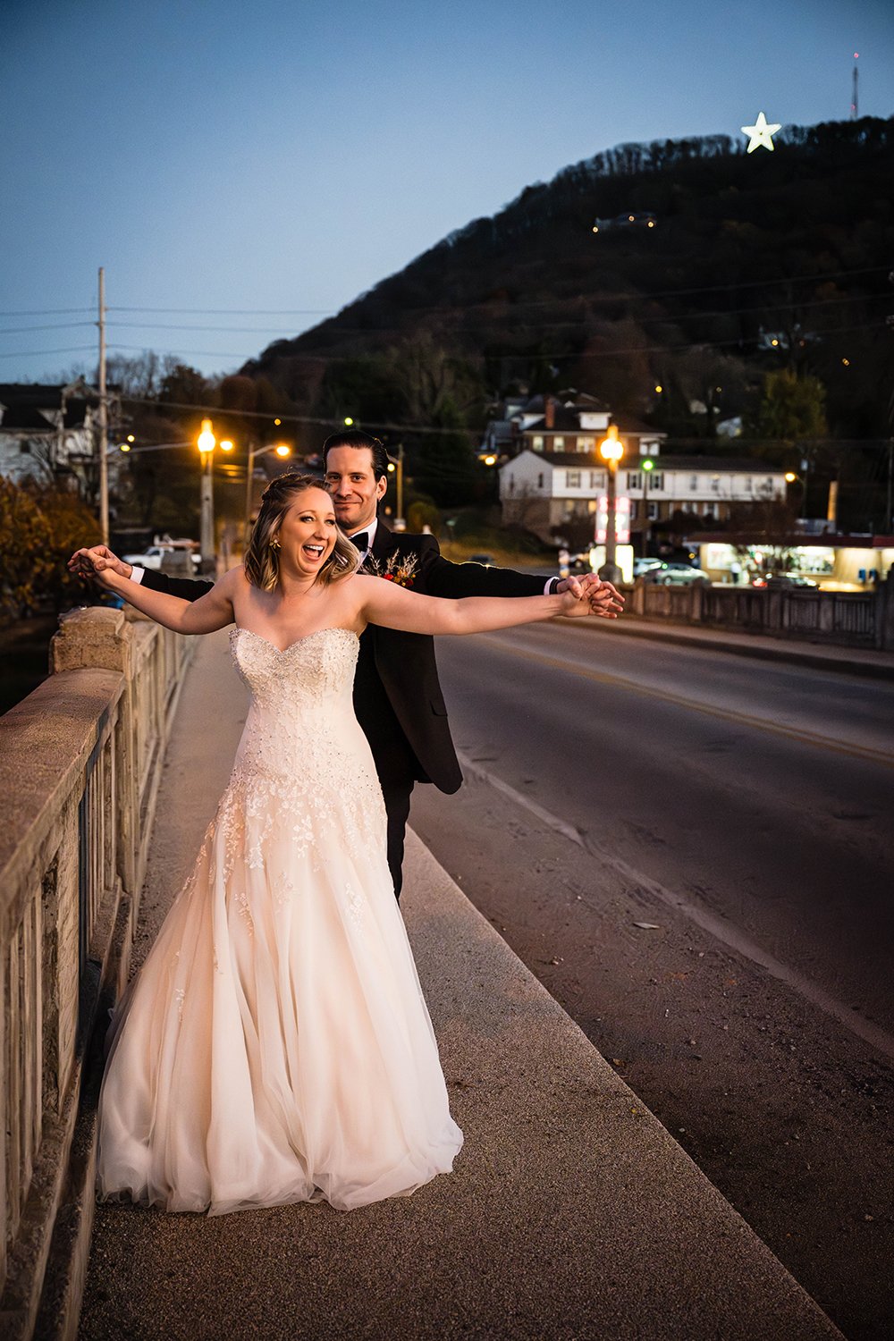A couple intertwines fingers and laughs as they’re given a funny prompt by the photographer on their elopement day on a bride with the Mill Mountain Star in the background.