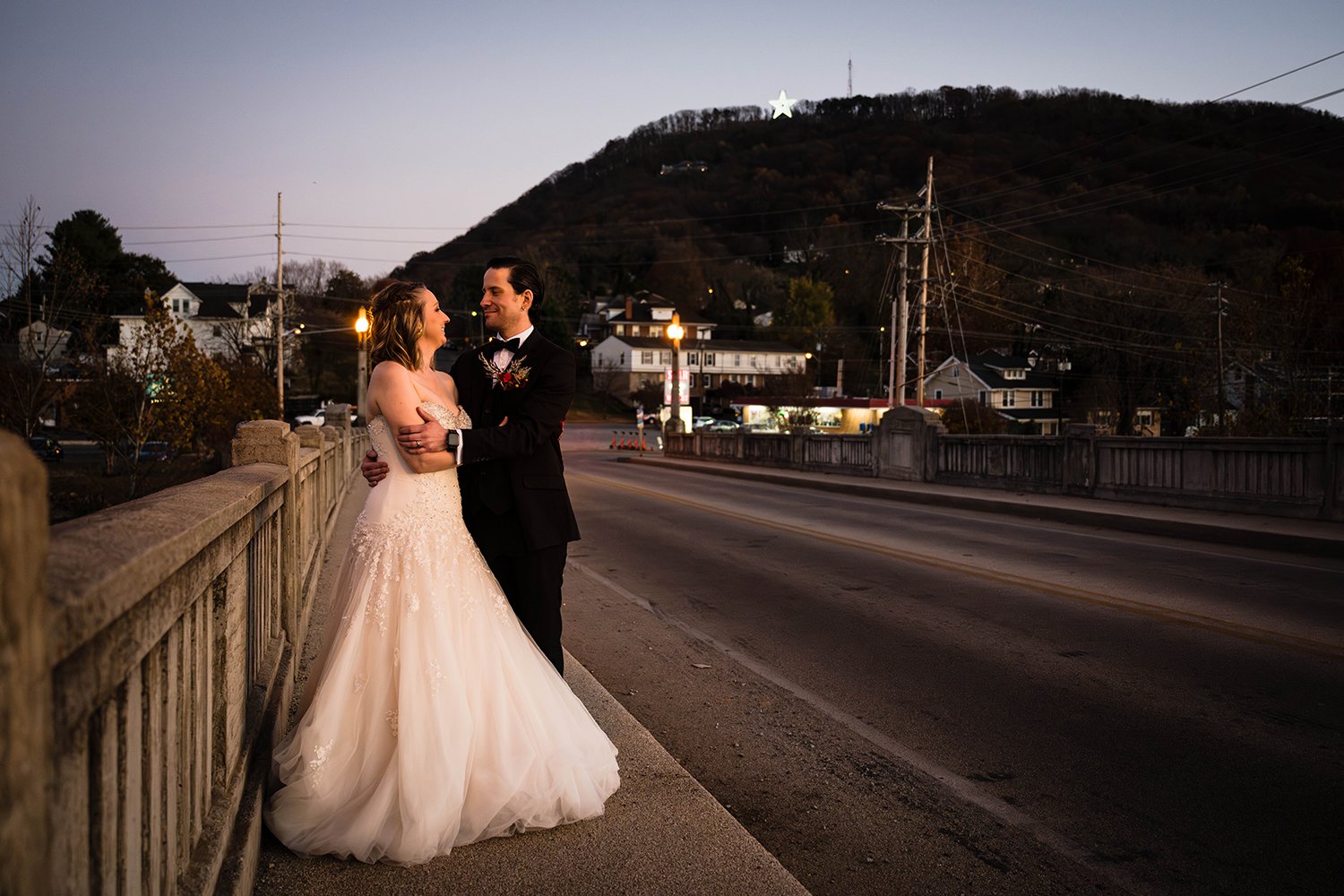 A couple on their elopement day embraces on a bridge leading up to Mill Mountain Star during blue hour in Roanoke, Virginia.