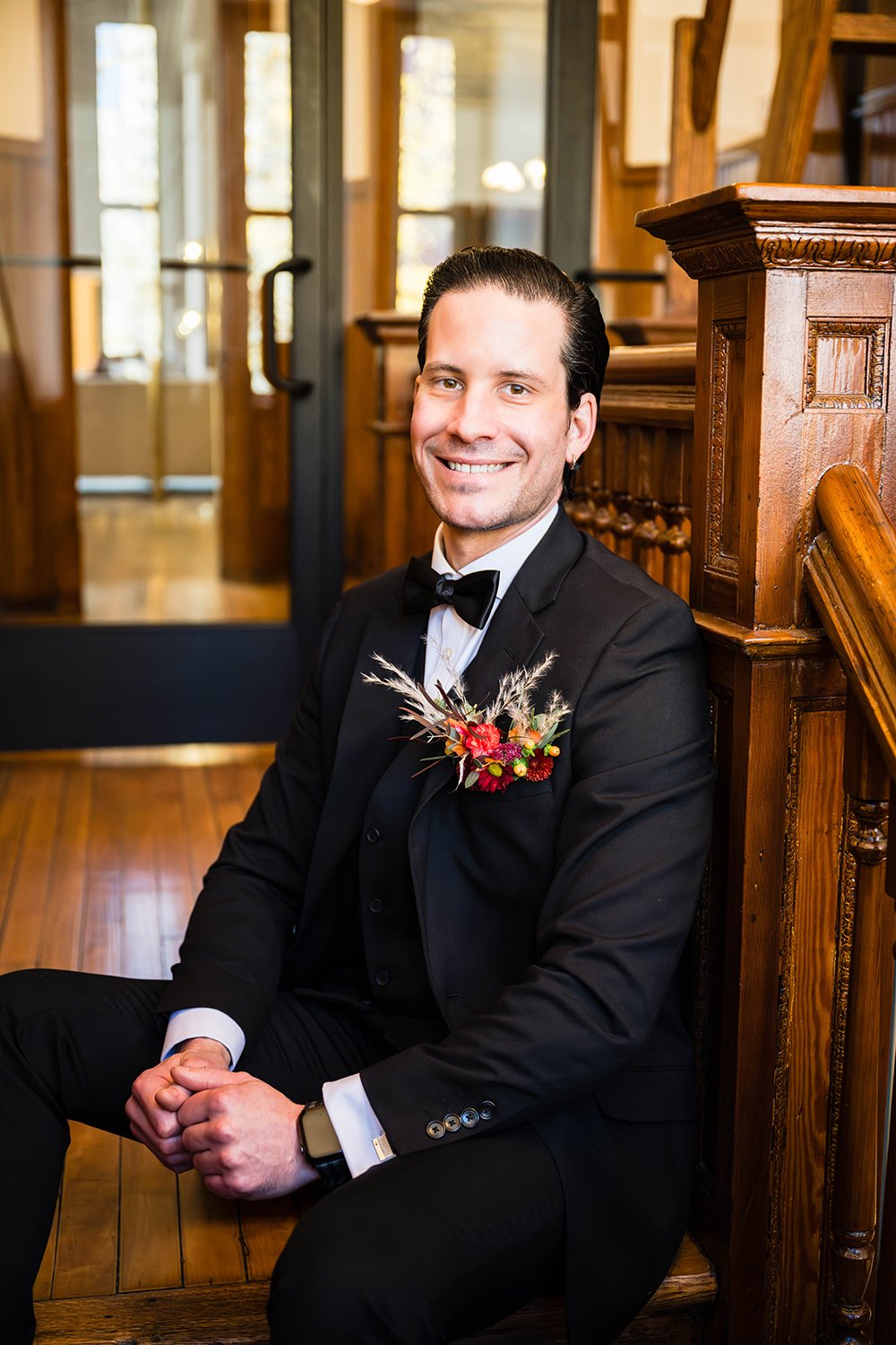  A marrier in a black suit sits in the stairwell of the Fire Station One Boutique Hotel and smiles for a photo on his elopement day. 