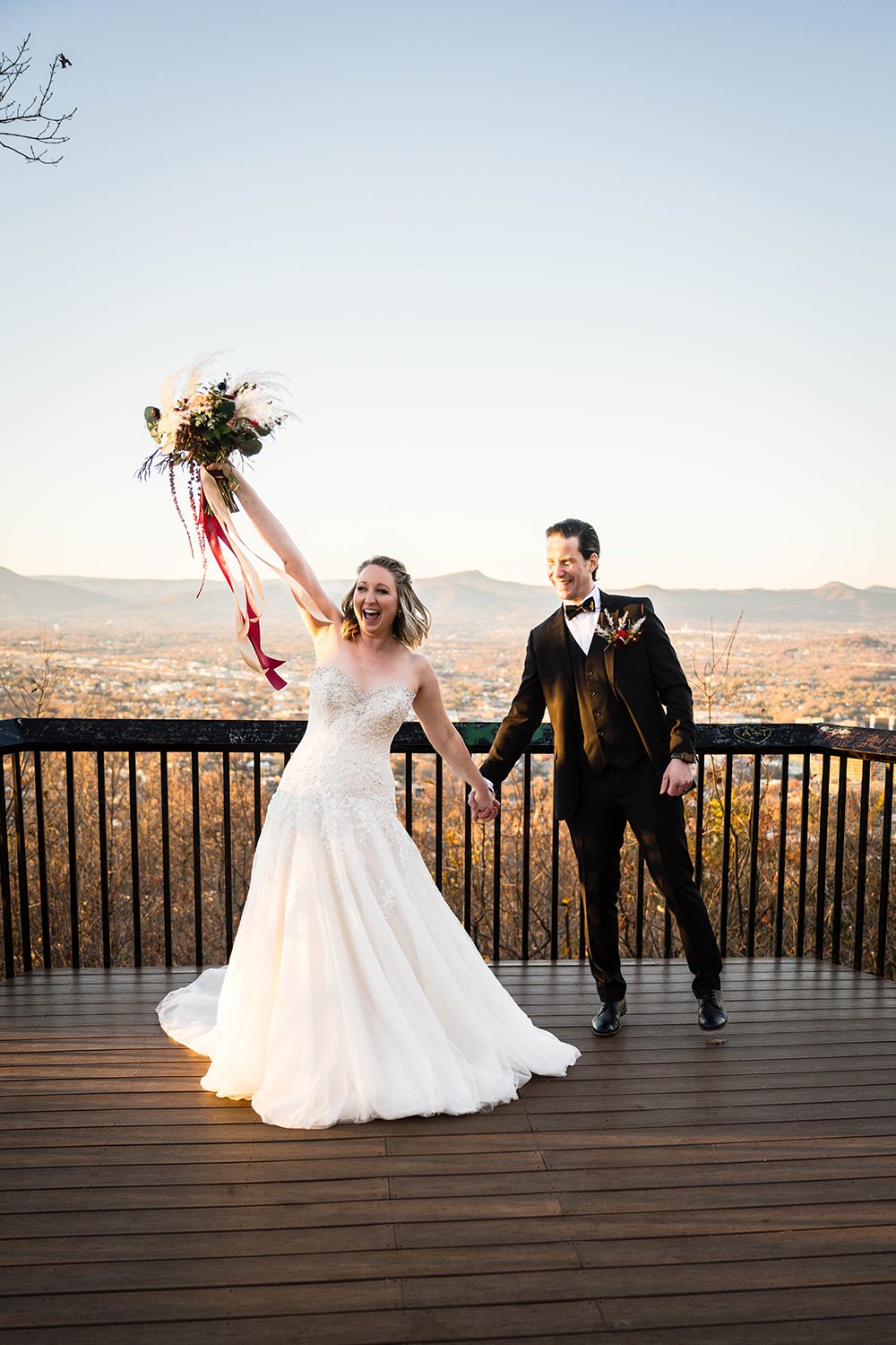 A bride and groom hold hands and cheer and smile excitedly after their elopement ceremony at the Mill Mountain Star overlook in Roanoke, Virginia.