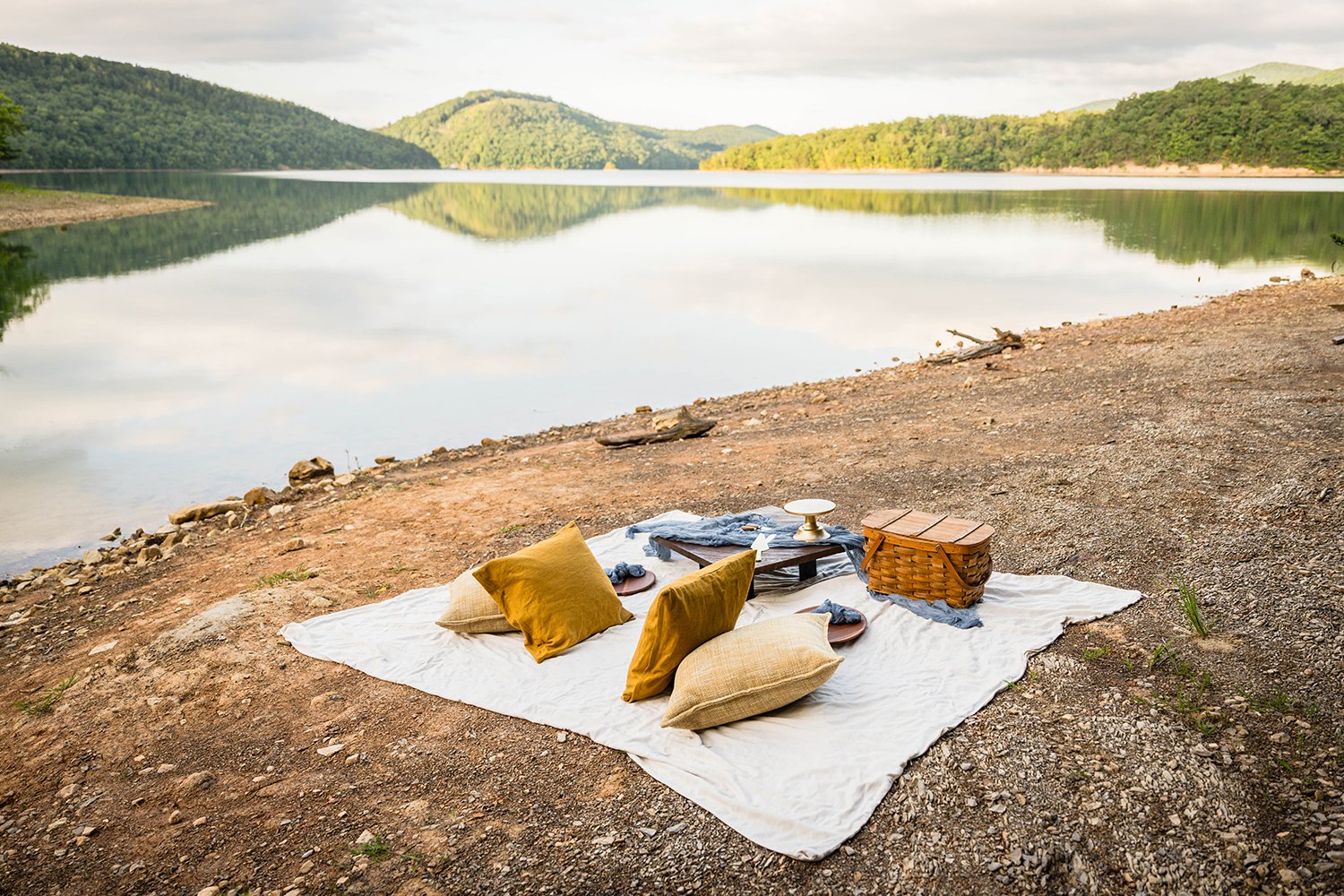 A boho picnic set up with wicker picnic basket on the coast of Carvin's Cove, which is near the Blue Ridge Parkway,
