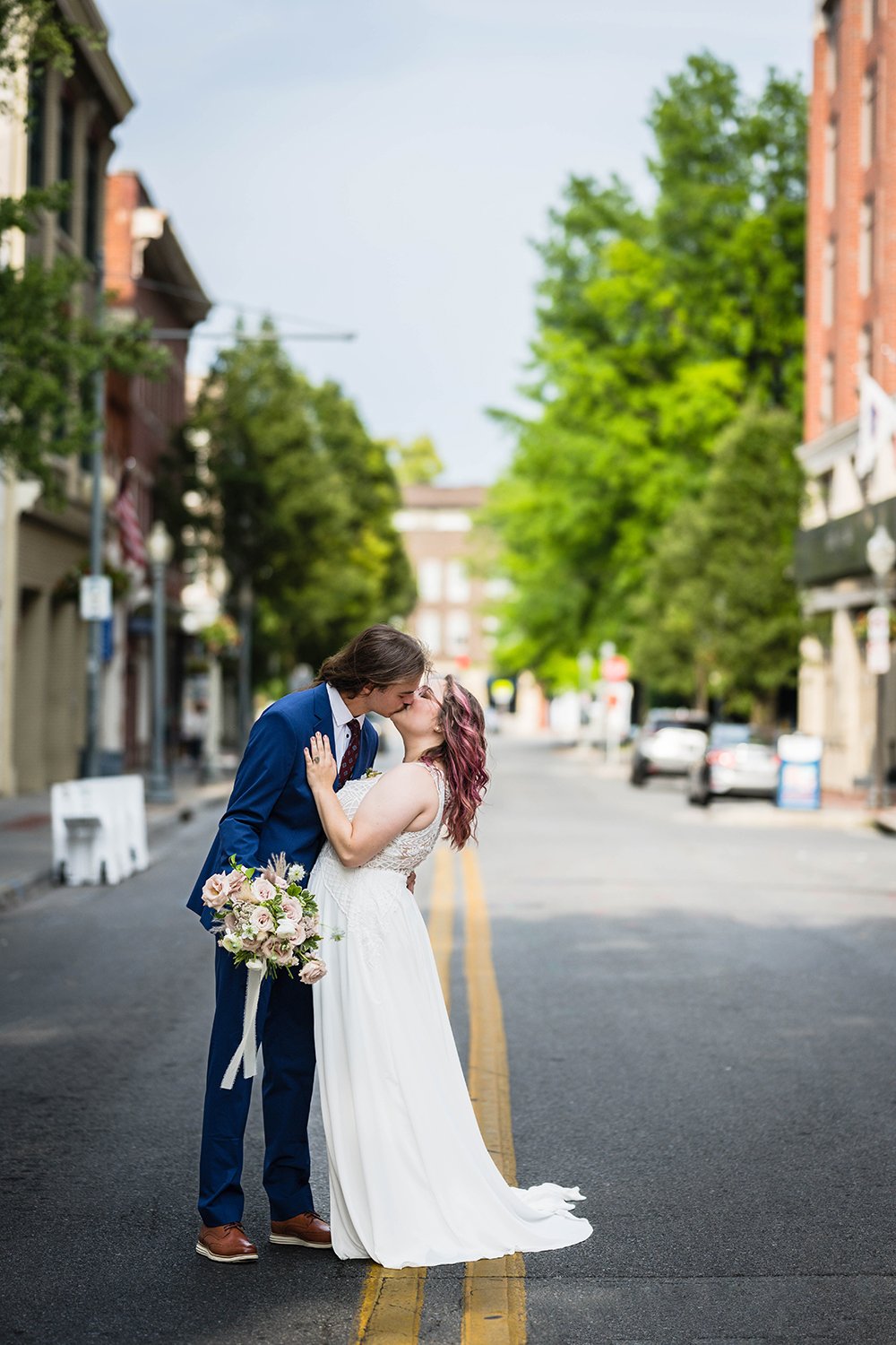A wedding couple on their elopement day embrace and kiss in the middle of the street in Downtown Roanoke in June.
