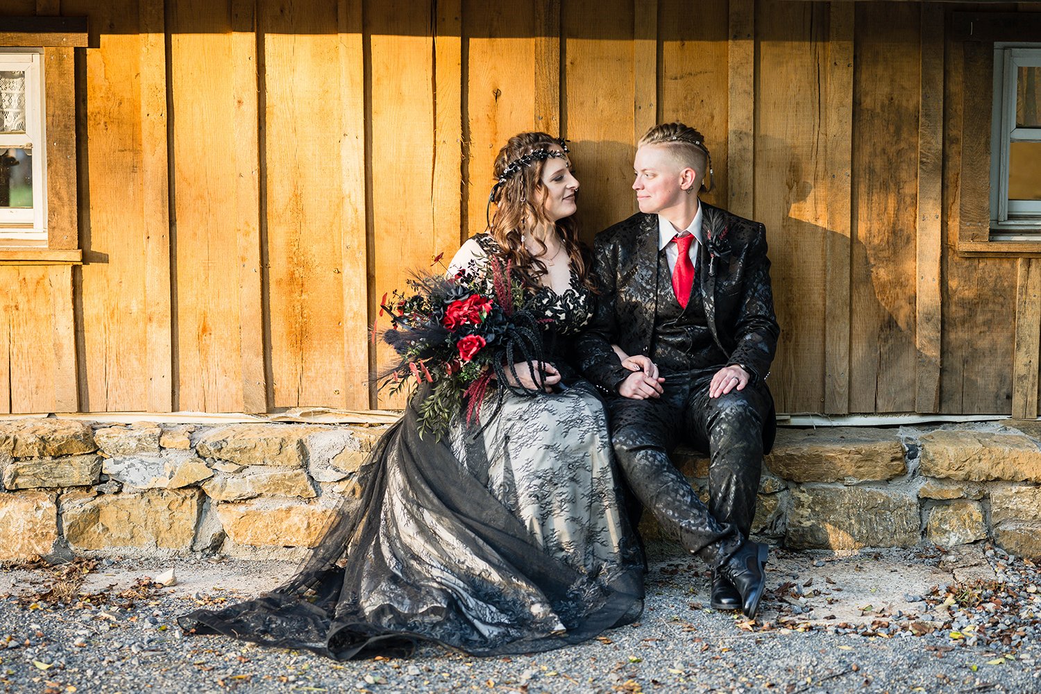 An LGBTQ+ couple sits against a ledge on the side of their Airbnb. The couple angles in towards one another and look contently at one another at the conclusion of their elopement day.