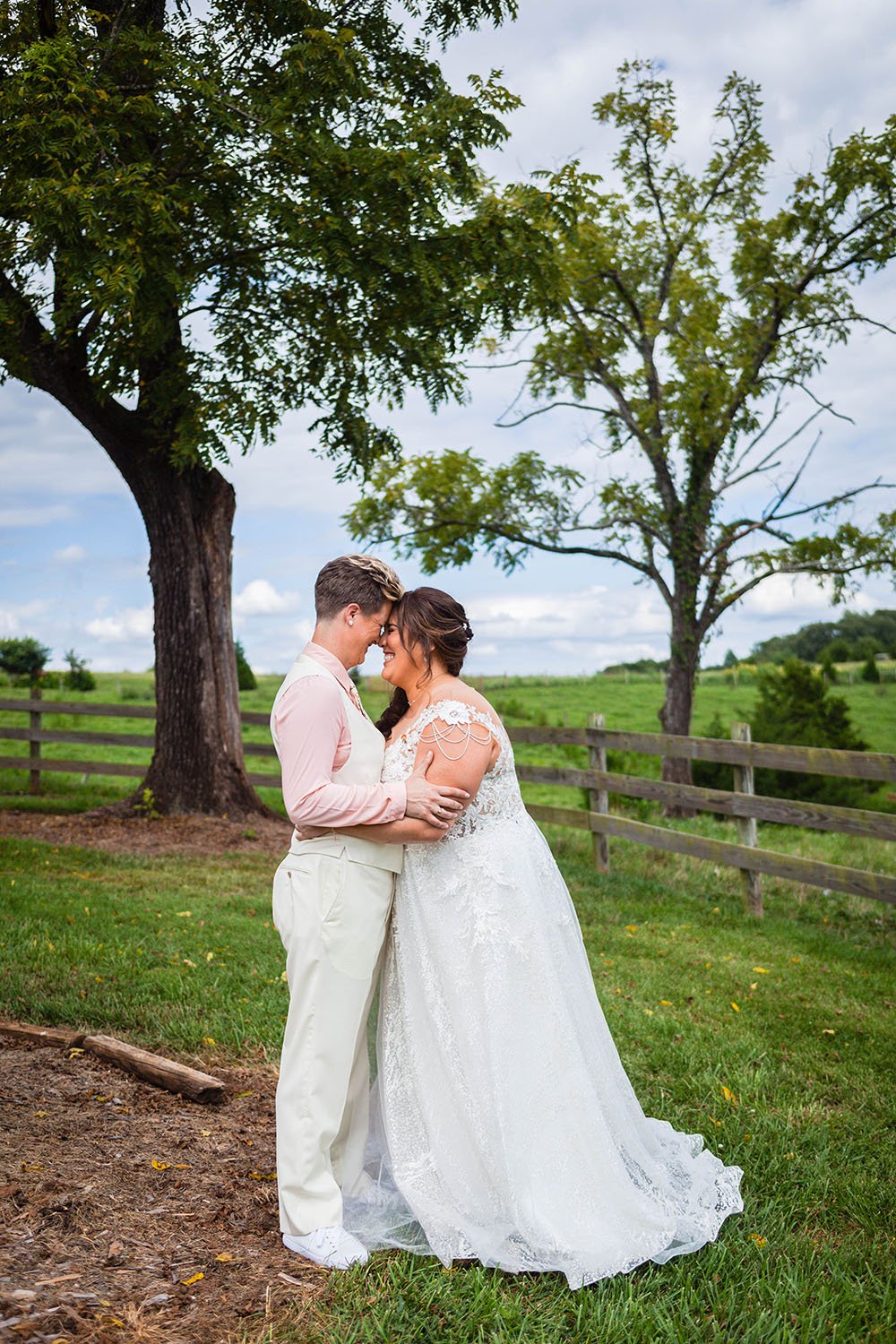 A lesbian couple embraces and puts their foreheads together as they smile and laugh on their summer elopement day in Virginia.