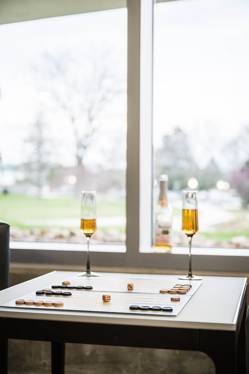 Two champagne flutes partially full of non-alcoholic cider sit atop a table with a Backgammon board game and dice set up.