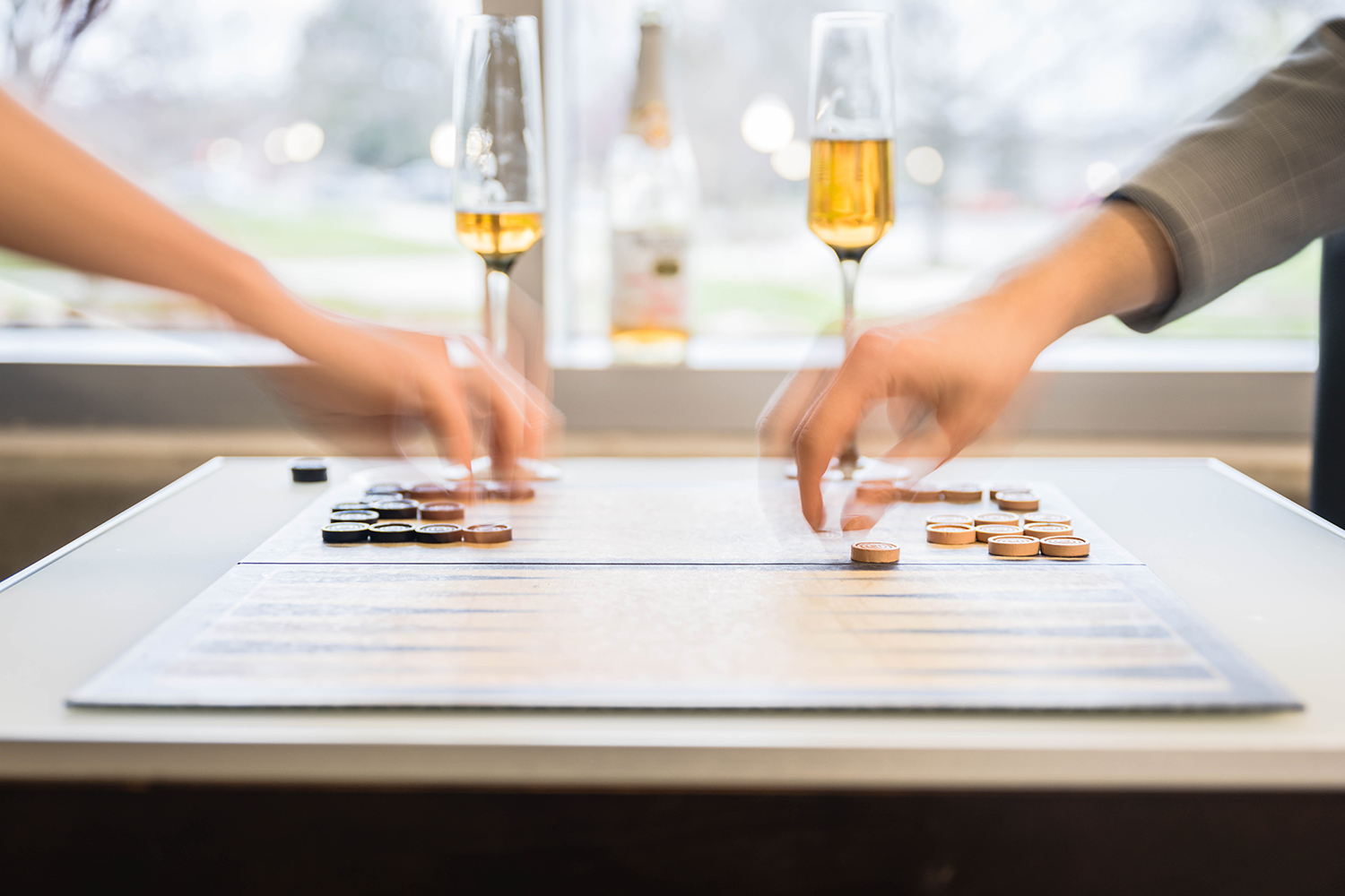 Two hands on opposite sides of a table moving pieces or dice during a Backgammon game. 