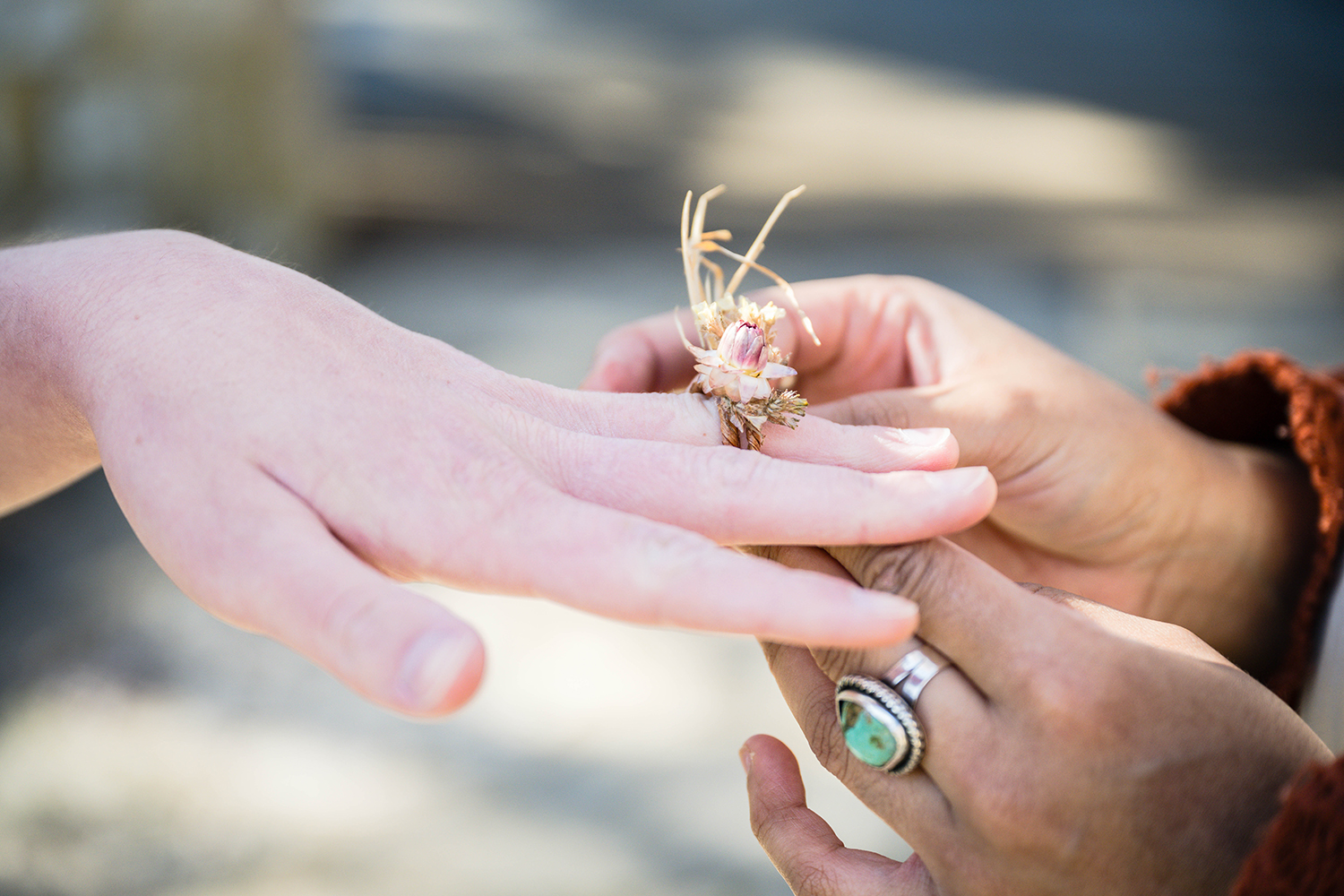 A queer marrier slides a dried flower ring onto their partner's hand during their elopement ceremony at Duck Pond.