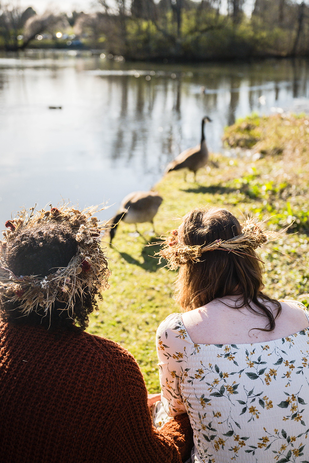 An LGBTQ+ couple crouches in front of two geese and observe them while holding onto one another.