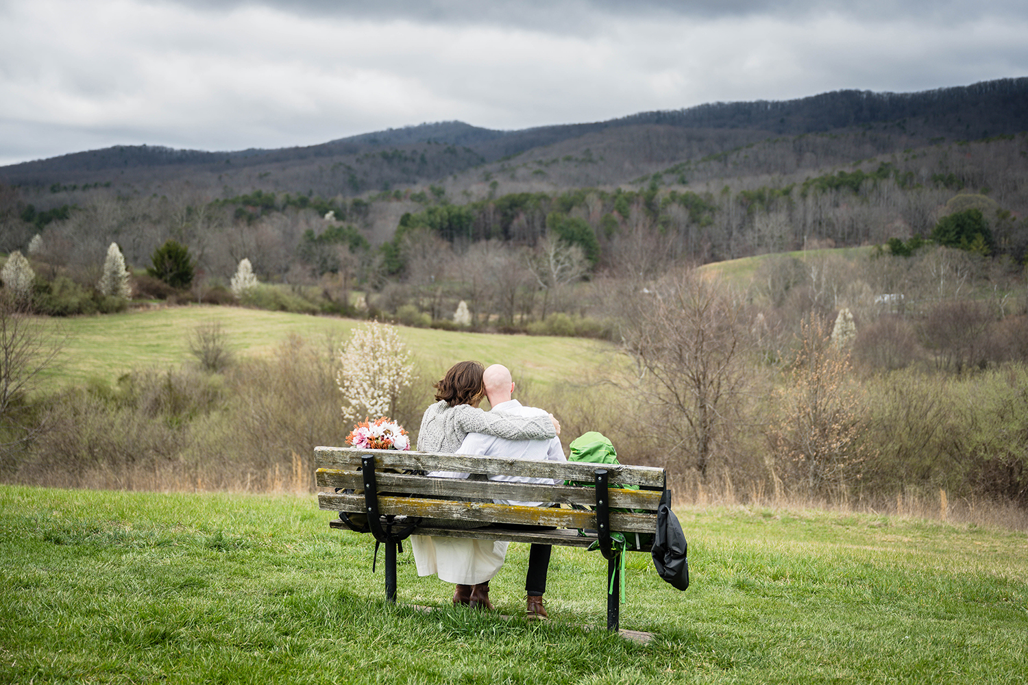 A couple on their elopement day sit at a bench overlooking the Blue Ridge Mountains at Heritage Park in Blacksburg, Virginia.