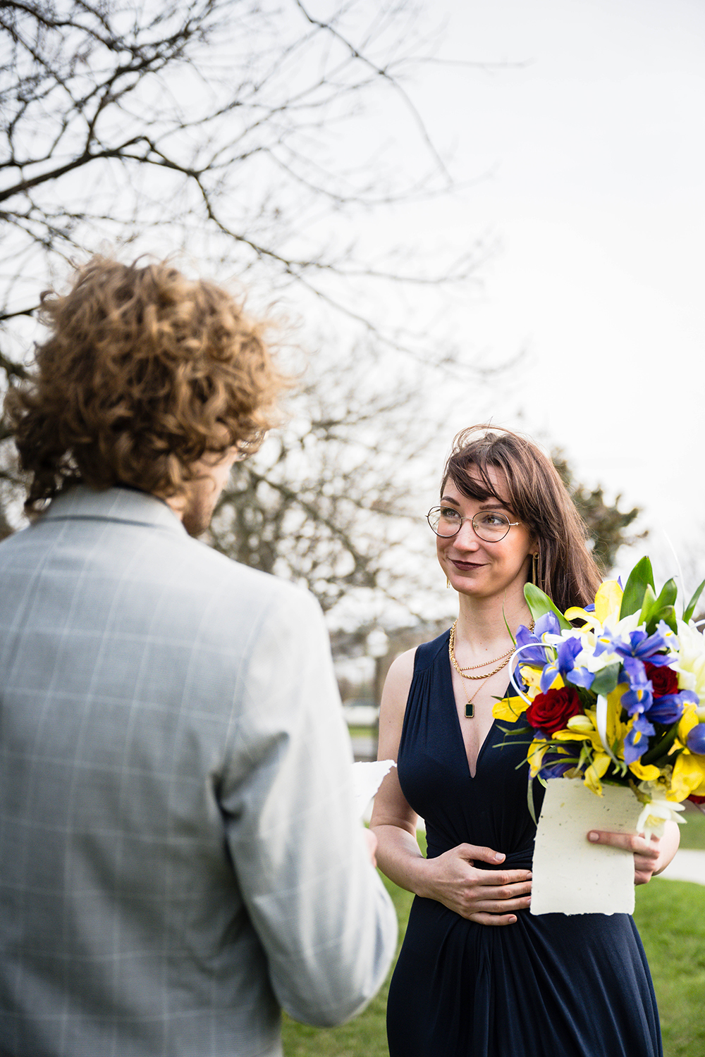 A marrier holds her bouquet and her vows and listens intently as her partner reads his vows to her on their elopement day.