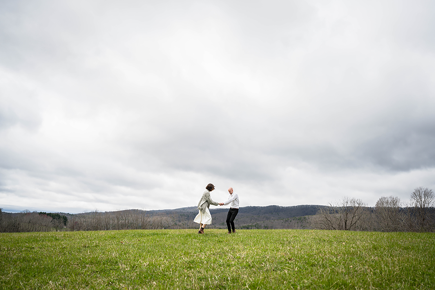 A couple dances atop of a hill with 360-degree views of the Blue Ridge Mountains on their elopement day at Heritage Park in Blacksburg, Virginia.