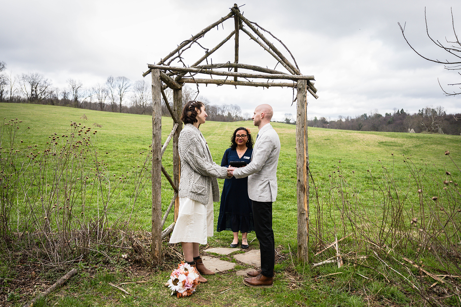 A couple hold hands under a make-shift altar with their officiant for their ceremony at Heritage Park in Blacksburg, Virginia.