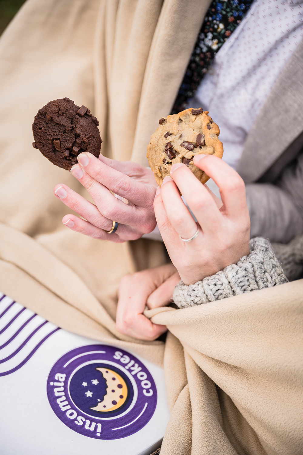 A couple on their elopement day cuddle under a blanket and show off their vegan cookies from Insomnia Cookies.