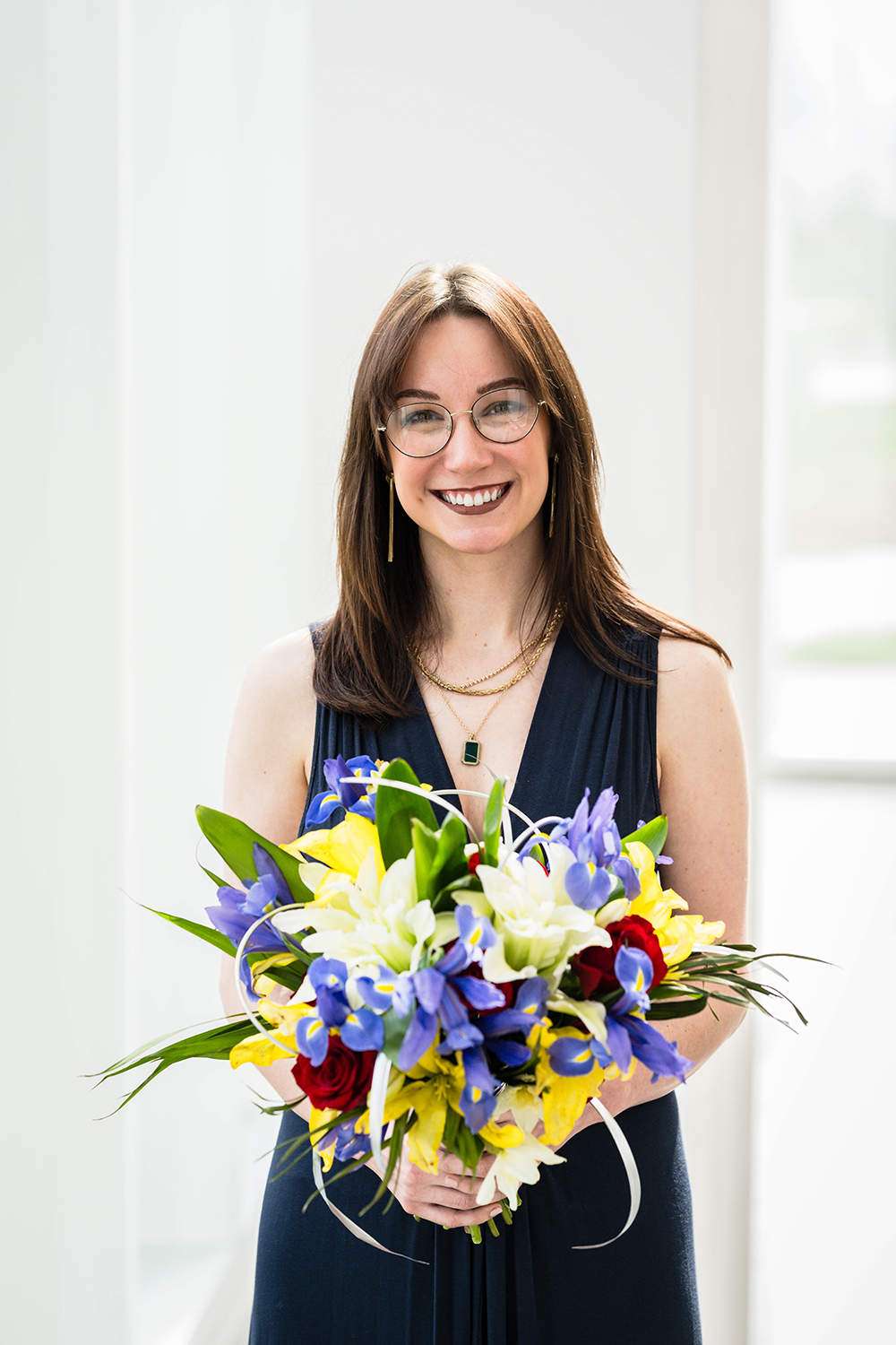 A bride wearing a non-traditional navy blue gown holds her bouquet in front of her and smiles for a portrait on her elopement day.