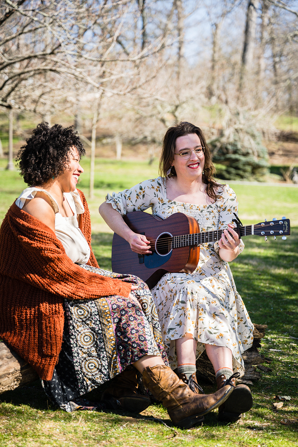 A transwoman plays a guitar and smiles as their queer partner laughs.
