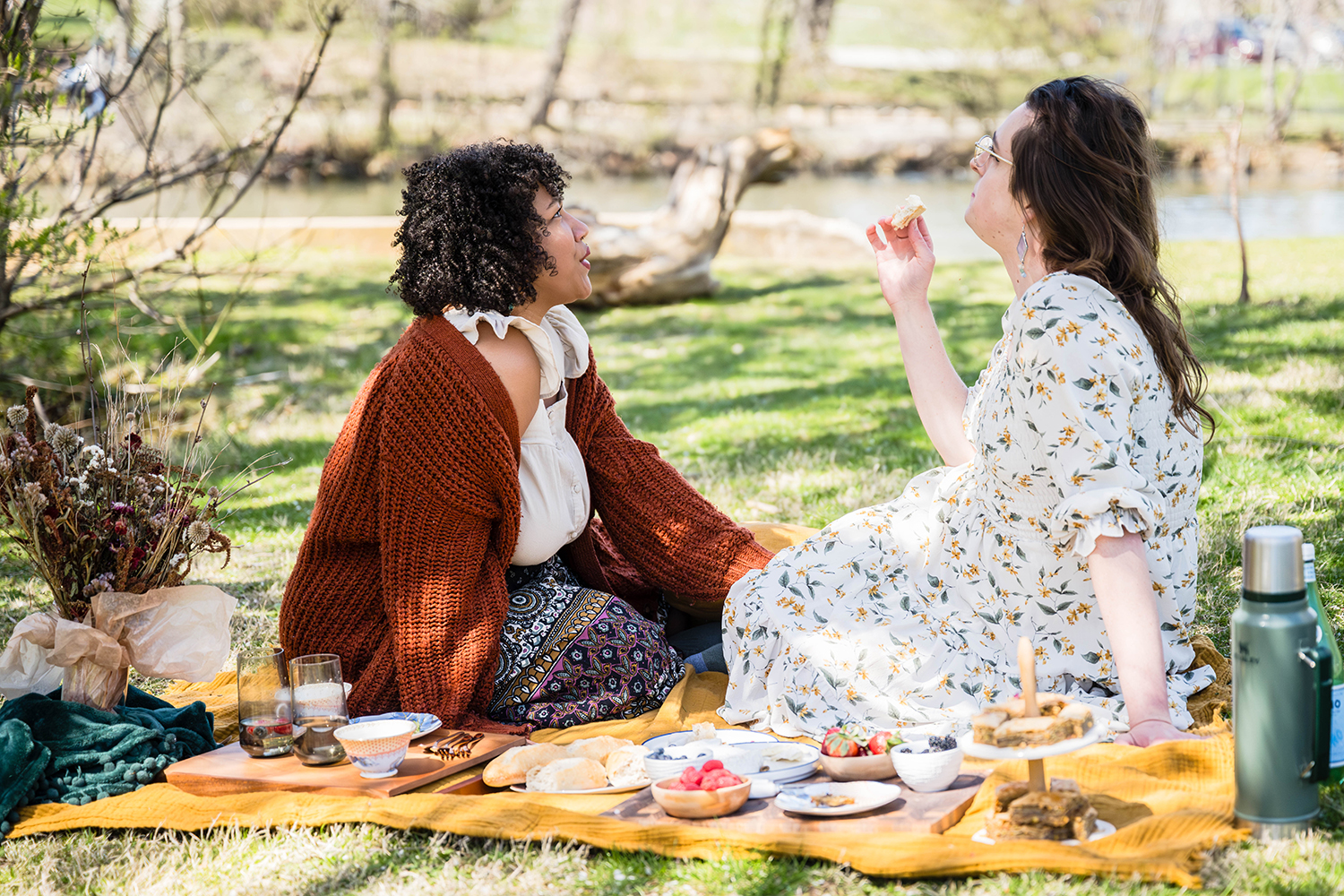 A queer couple have a picnic at Duck Pond and look up towards the trees as they talk and eat.