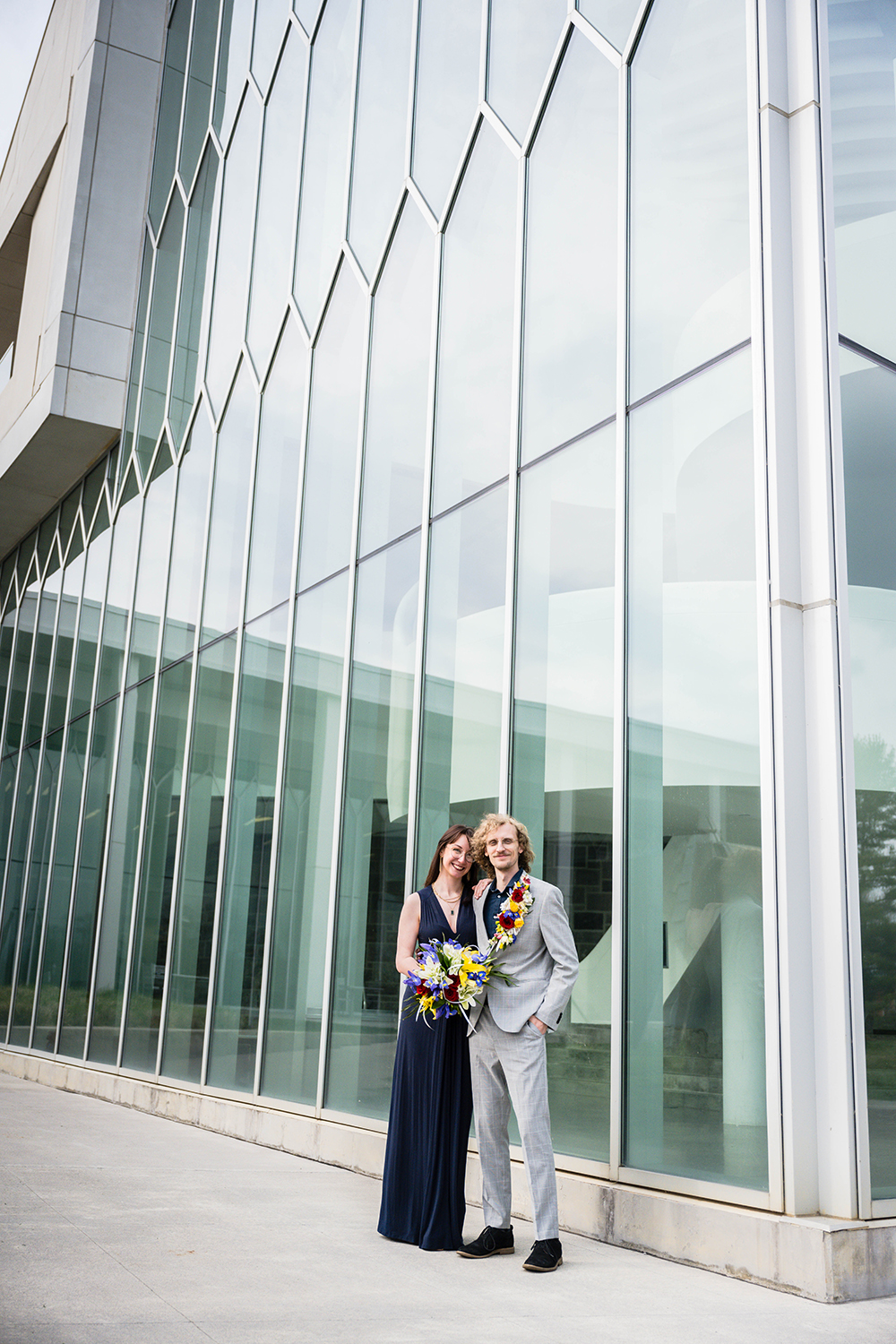 A newlywed couple poses together in front of the iconic windows of the Moss Arts Center.