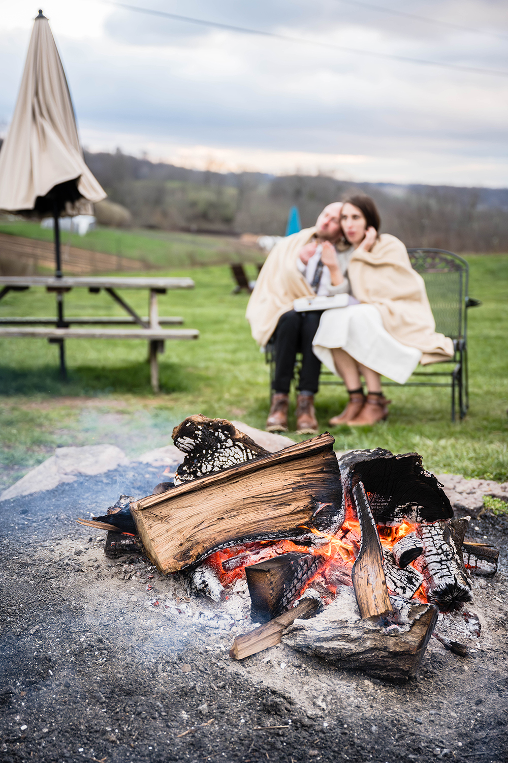 A couple cuddle under a blanket and sit behind a fire at Rising Silo Brewery eating cookies.