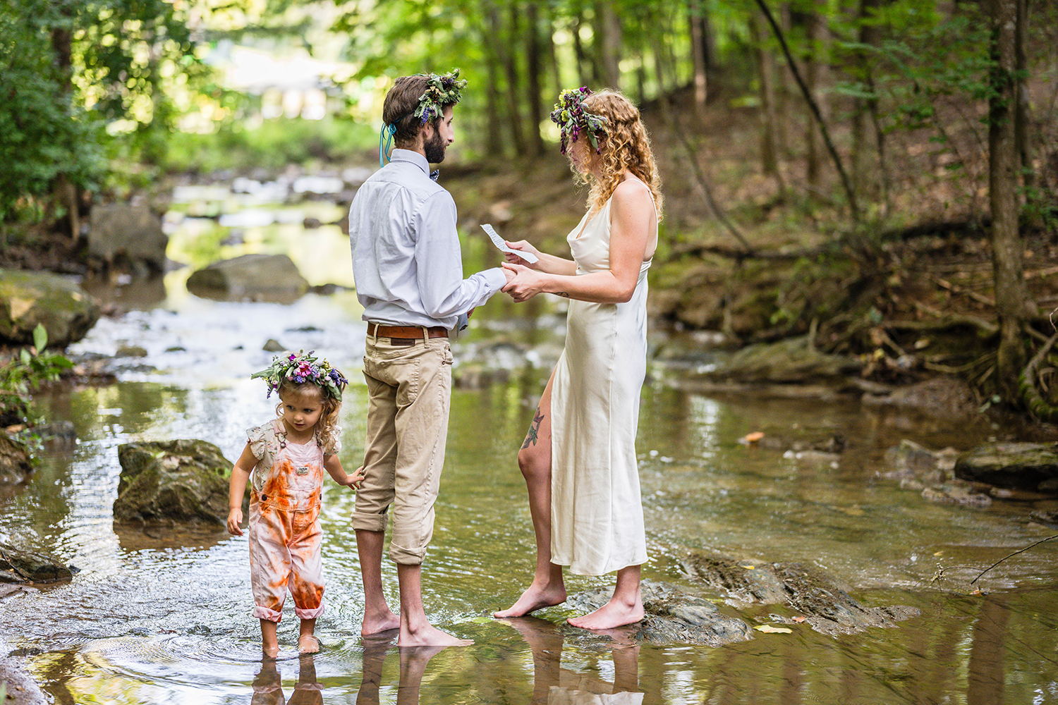 A couple renews their vows in the shallow waters at Fishburn Park in Roanoke, Virginia. A small child tugs at her parent's pants to try to get their attention.