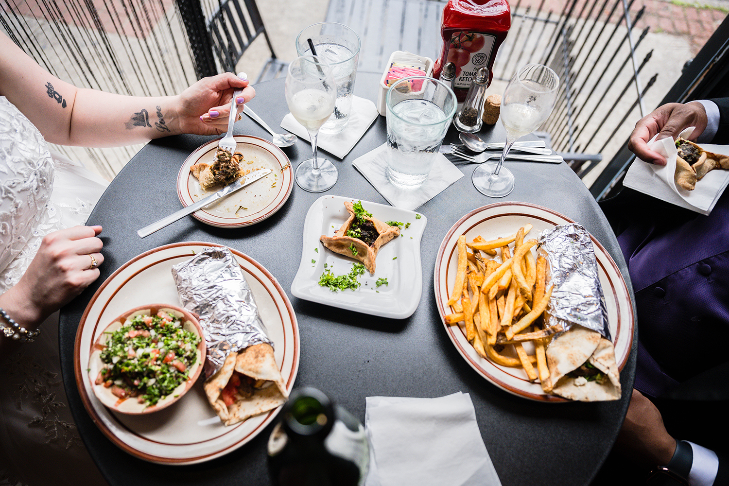 A couple sits at a table at Cedar's Lebanese Restaurant for dinner. The photo is taken from a birds-eye view and shows various plates with various foods and water and wine glasses spread on the table.